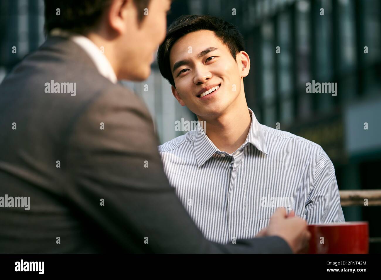 Zwei asiatische Geschäftsleute, die bei einem Kaffee im Freien über Geschäfte diskutieren Kaufen Stockfoto