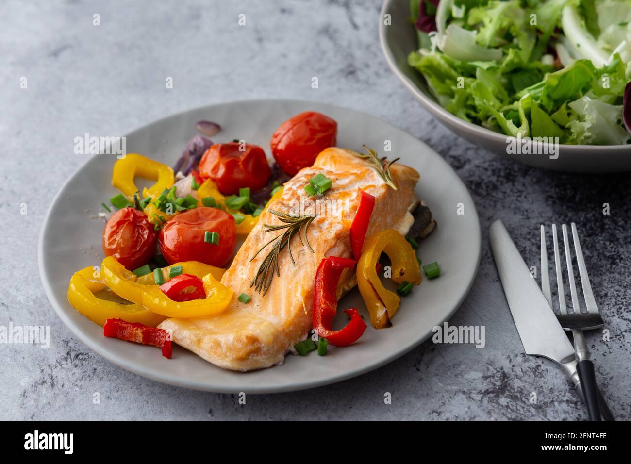 Gebackenes rotes Fischfilet Arctic Saibling auf einem Teller mit Gemüse, Salat in einer Schüssel mischen, leckeres herzhaftes gesundes Abendessen Stockfoto