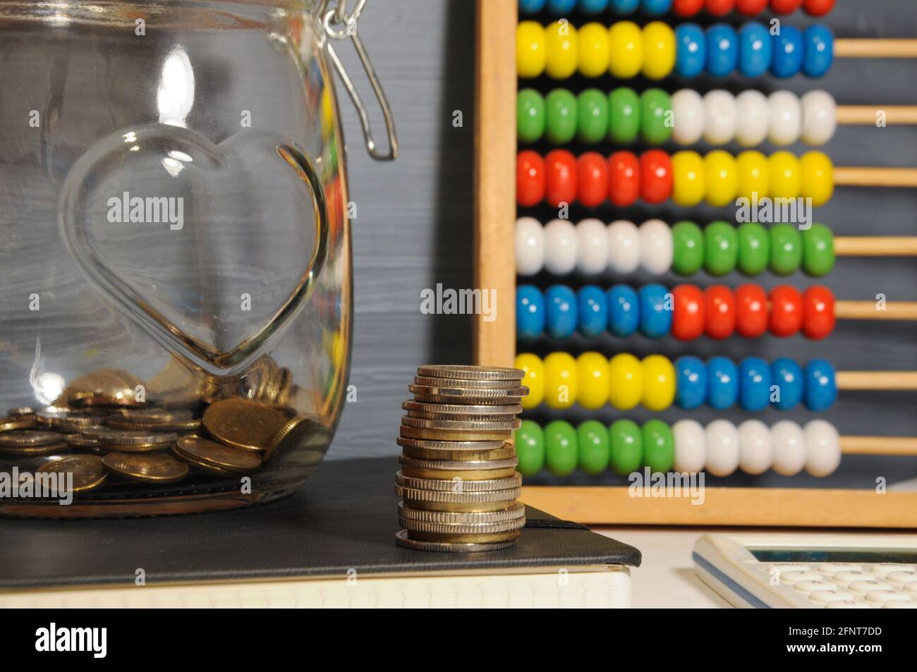 Stapel von Goldmünzen, Glas und bunten Abakus auf dem grauen Hintergrund - Geld sparen Stockfoto