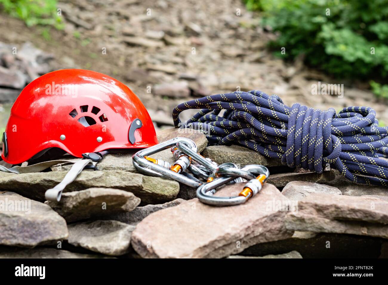 Seilzugangswerkzeuge: Schutzhelm, Seil, Karabiner. Bergsport Ausrüstung auf Felsen vor einem Hintergrund von Felsen und Grün Stockfoto