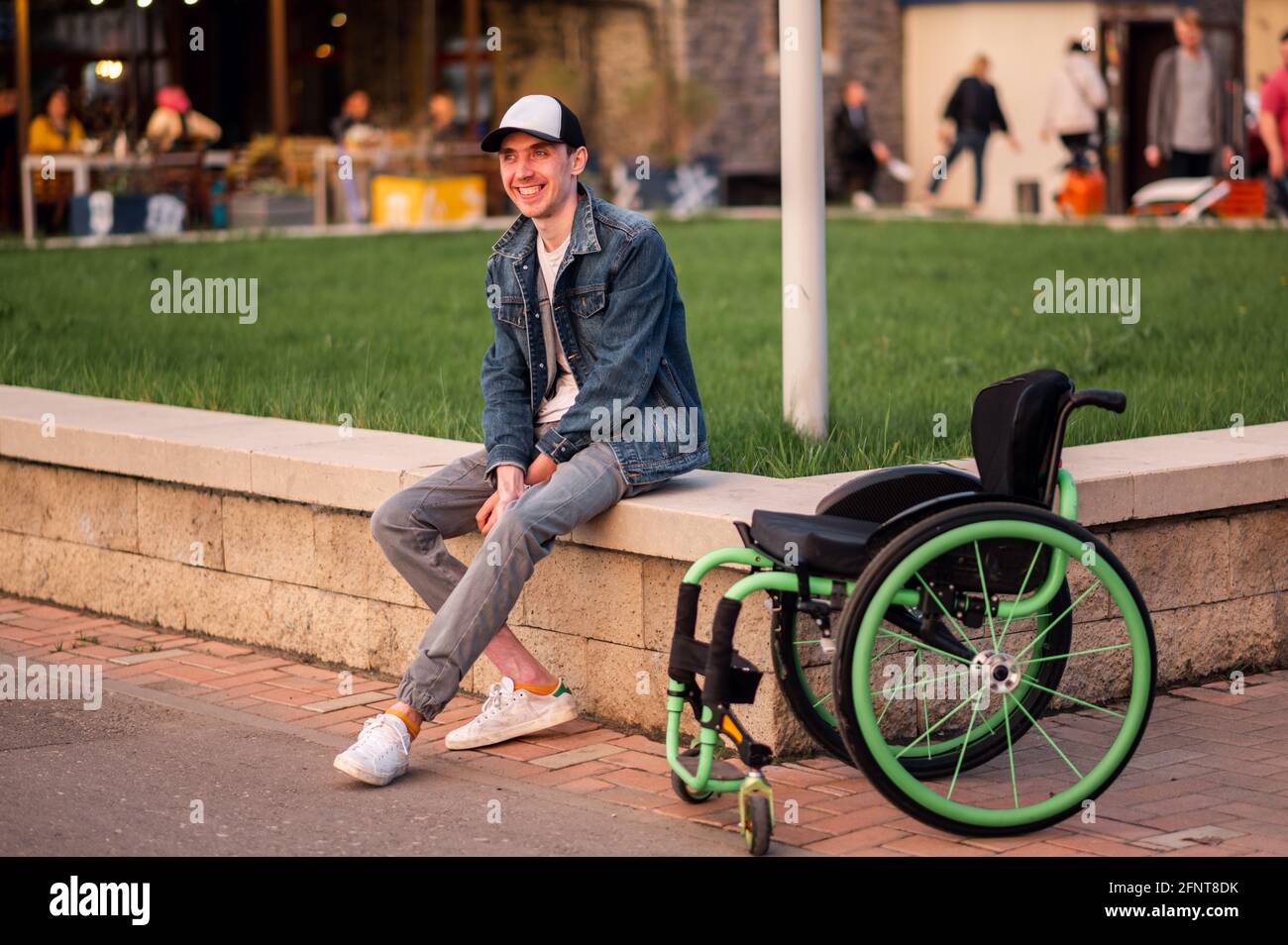 Ein junger behinderter Mann sitzt neben einem Rollstuhl und zeigt ihr den Mittelfinger Stockfoto