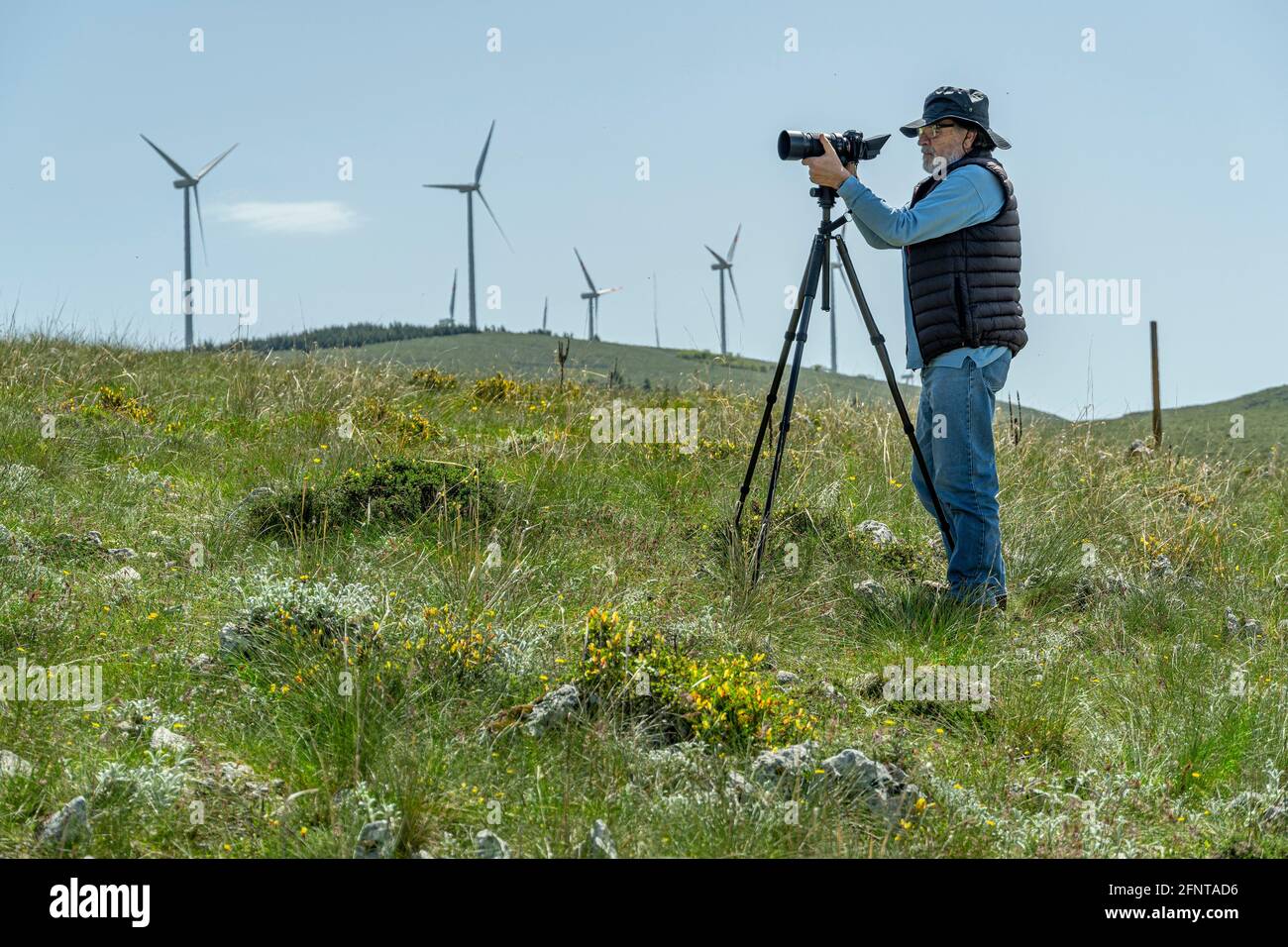 Älterer Mann mit neuer Technologie. Kamera auf Stativ, lässig gekleideter Mann. Windturbinen im Hintergrund. Abruzzen, Italien, Europa Stockfoto
