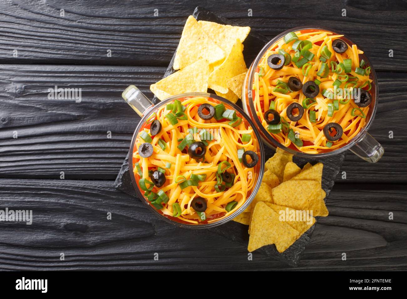 Klassisches mexikanisches 7-Schicht-Dip mit Maischips aus der Nähe im Glas auf dem Tisch. Horizontale Draufsicht von oben Stockfoto