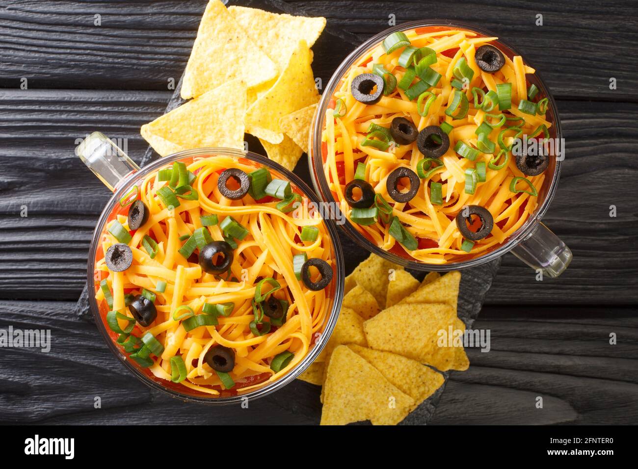 Seven-Layer Dip ist eine amerikanische Vorspeise, die auf typischen Zutaten der Tex-Mex-Küche aus nächster Nähe im Glas auf dem Tisch basiert. Horizontale Ansicht von oben Stockfoto