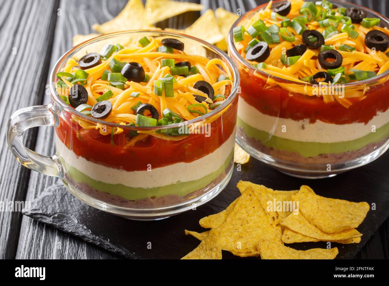 Klassisches mexikanisches 7-Schicht-Dip mit Maischips aus der Nähe im Glas auf dem Tisch. Horizontal Stockfoto