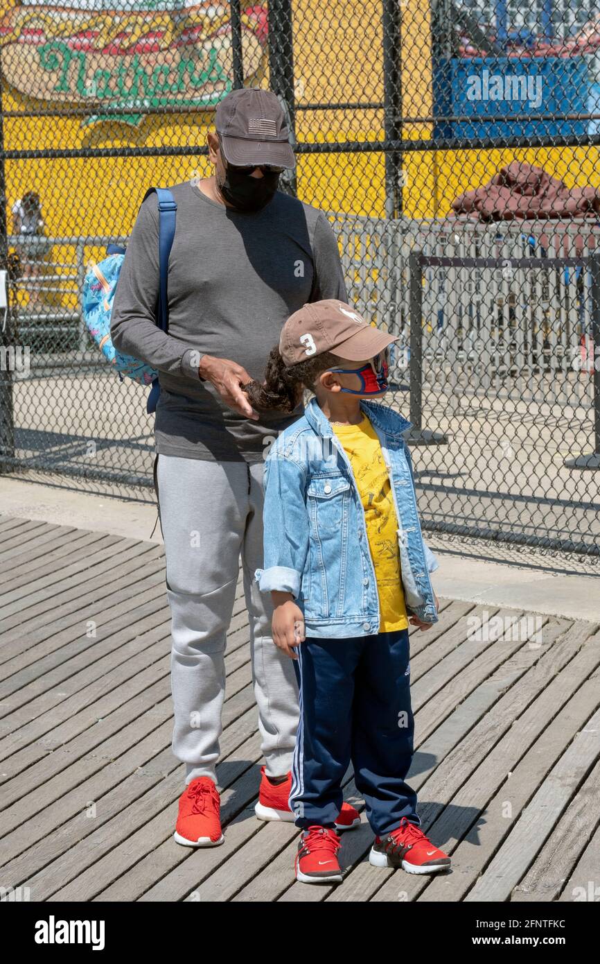 Ein Großvater hilft seiner Enkelin auf dem Boardwalk in Coney Island, Brooklyn, New York, die Haare zu flechtern. Stockfoto