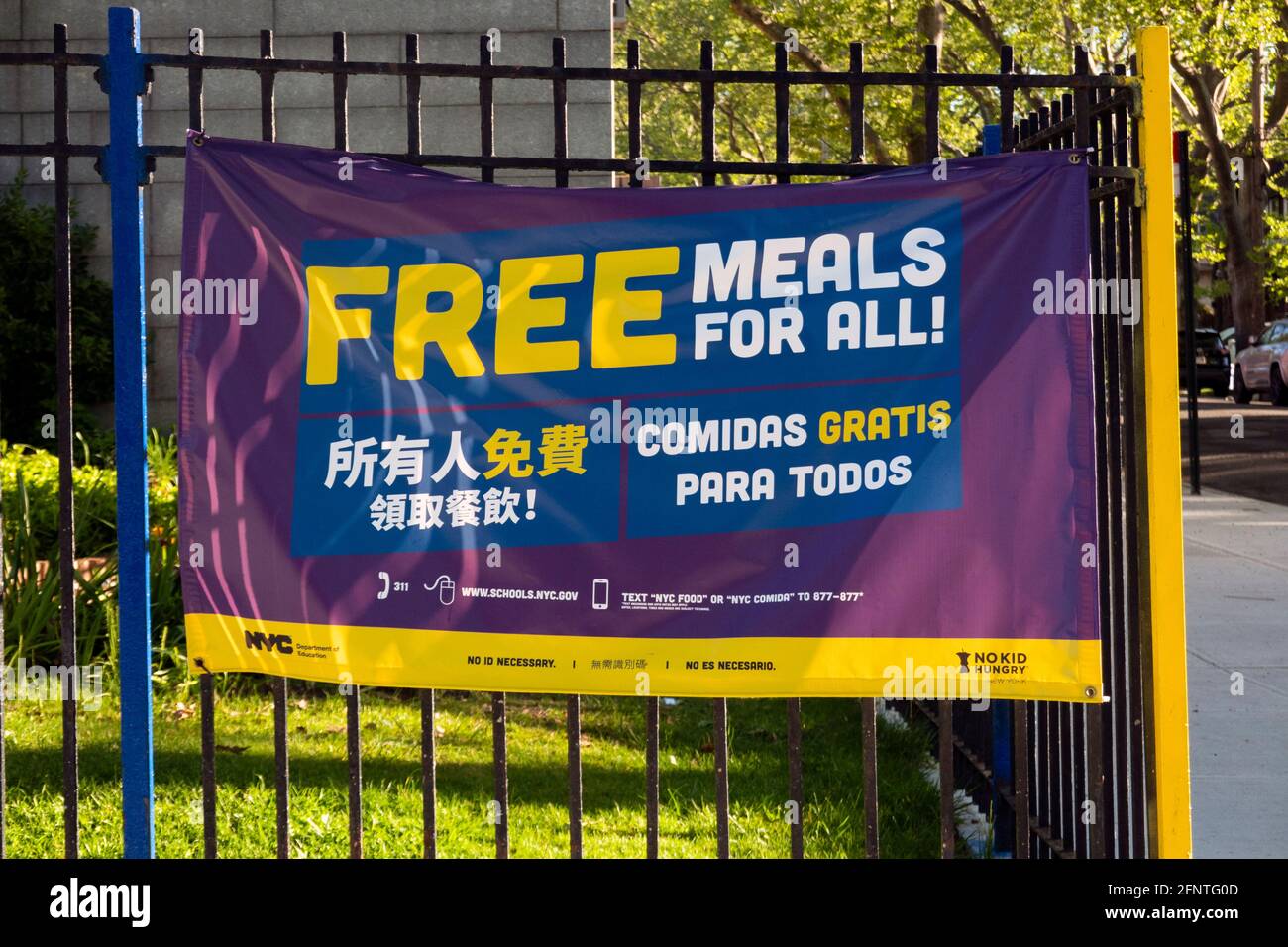 Ein dreisprachiges Schild an einem Zaun vor PS 32, das ein Programm für kostenlose Mahlzeiten für alle Kinder fördert. In Flushing, Queens, New York City. Stockfoto
