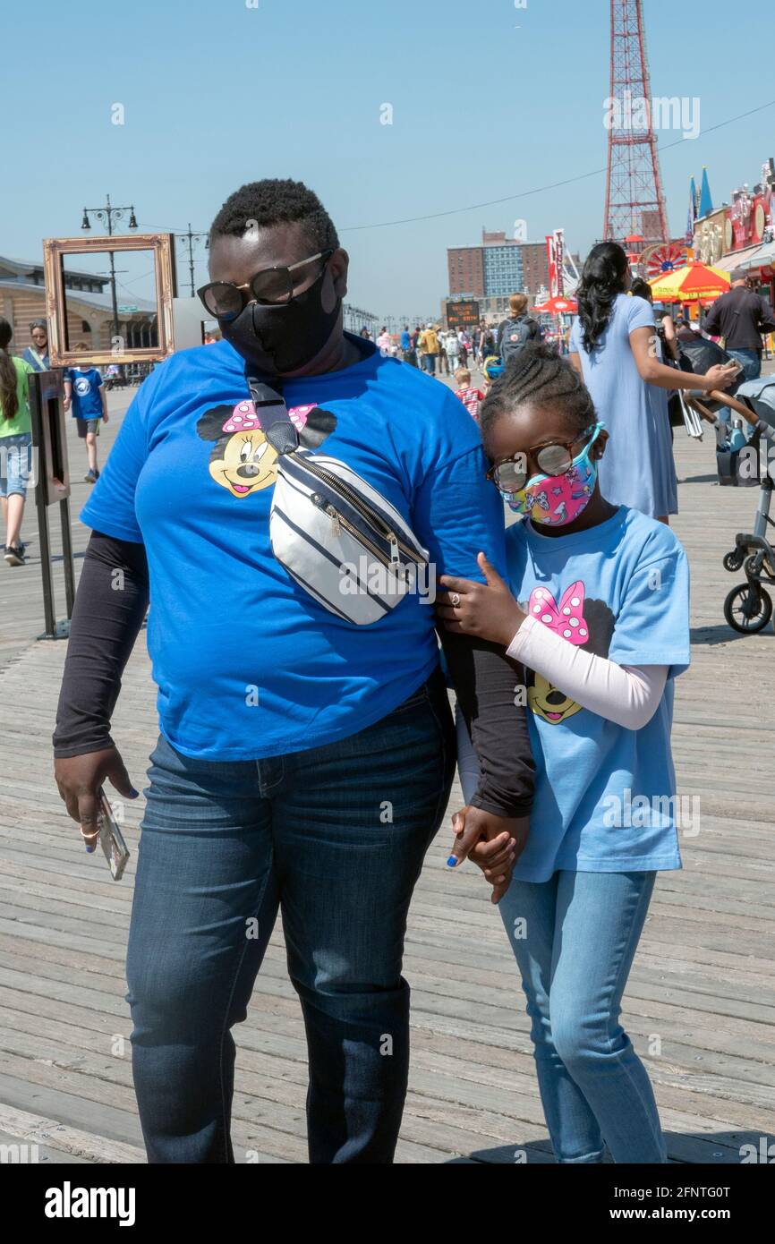 Eine Mutter und Tochter mit passenden Minnie Mouse T-Shirts laufen gemeinsam auf dem Boardwalk in Coney Island, Brooklyn, New York. Stockfoto