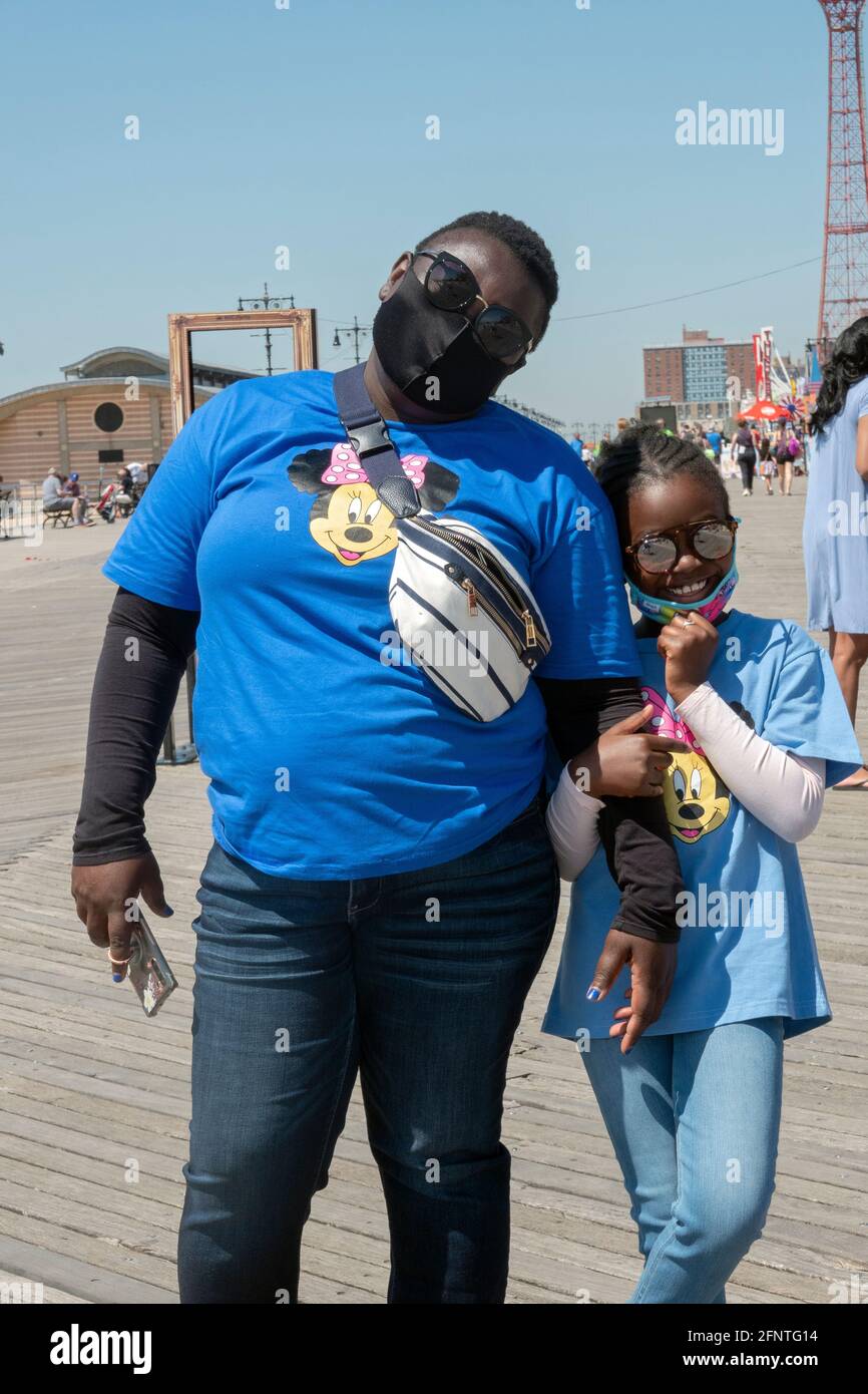 Eine Mutter und Tochter mit passenden Minnie Mouse T-Shirts laufen gemeinsam auf dem Boardwalk in Coney Island, Brooklyn, New York. Stockfoto