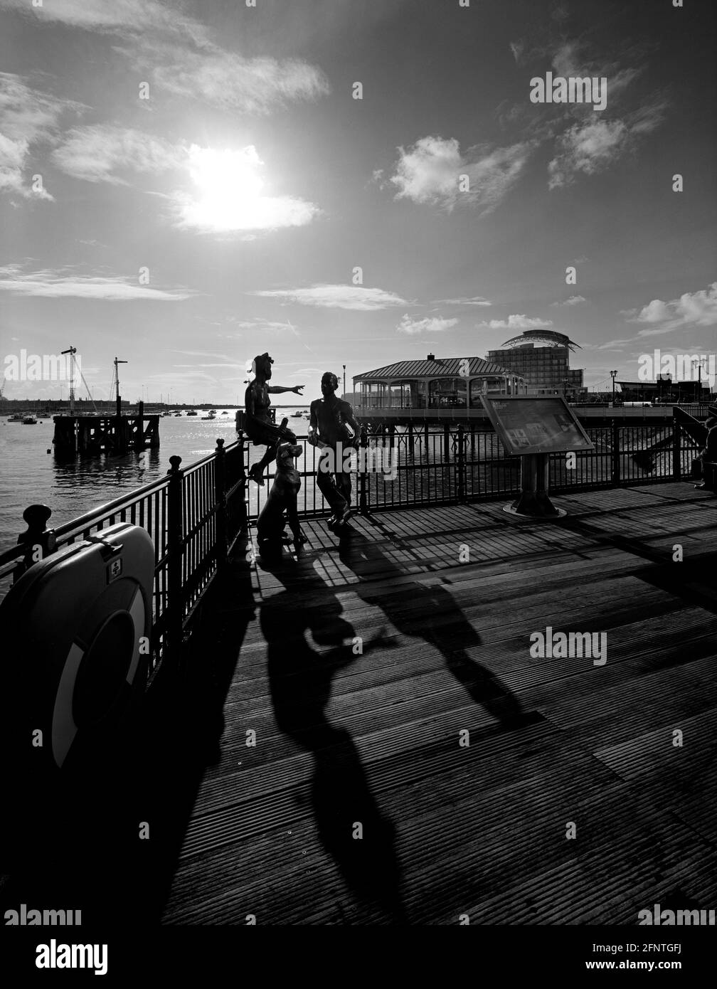 Schwarz-Weiß-Hochformat Menschen mögen uns Bronzeskulptur Mermaid Quay Cardiff Wales UK St David's Hotel im Hintergrund Junges Paar und Hund Stockfoto