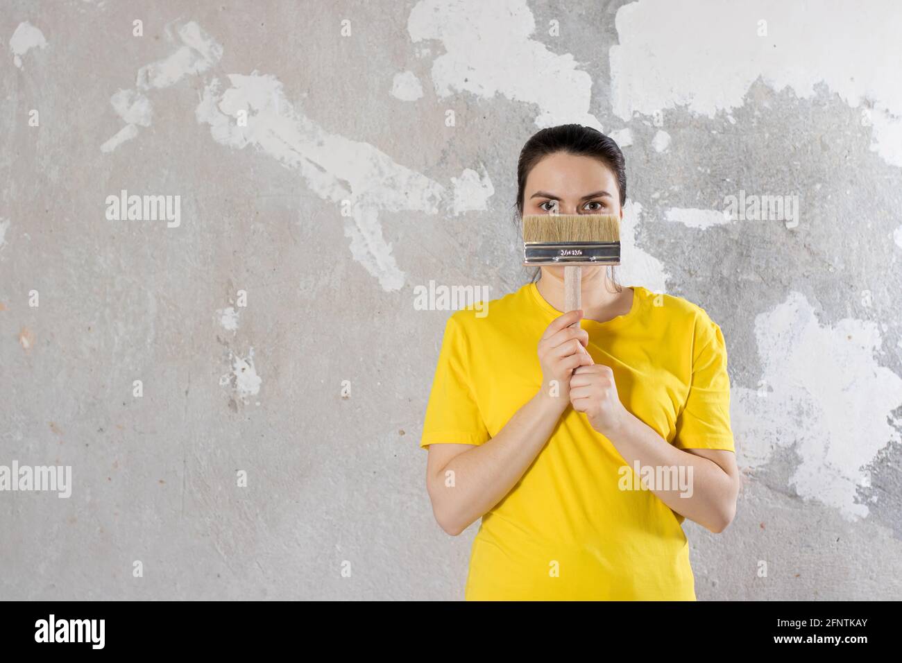 Eine Reparaturfrau in einem gelben, hellen T-Shirt hält einen Pinsel. Für Text platzieren. Schlüsselfertige Reparaturen. Stockfoto