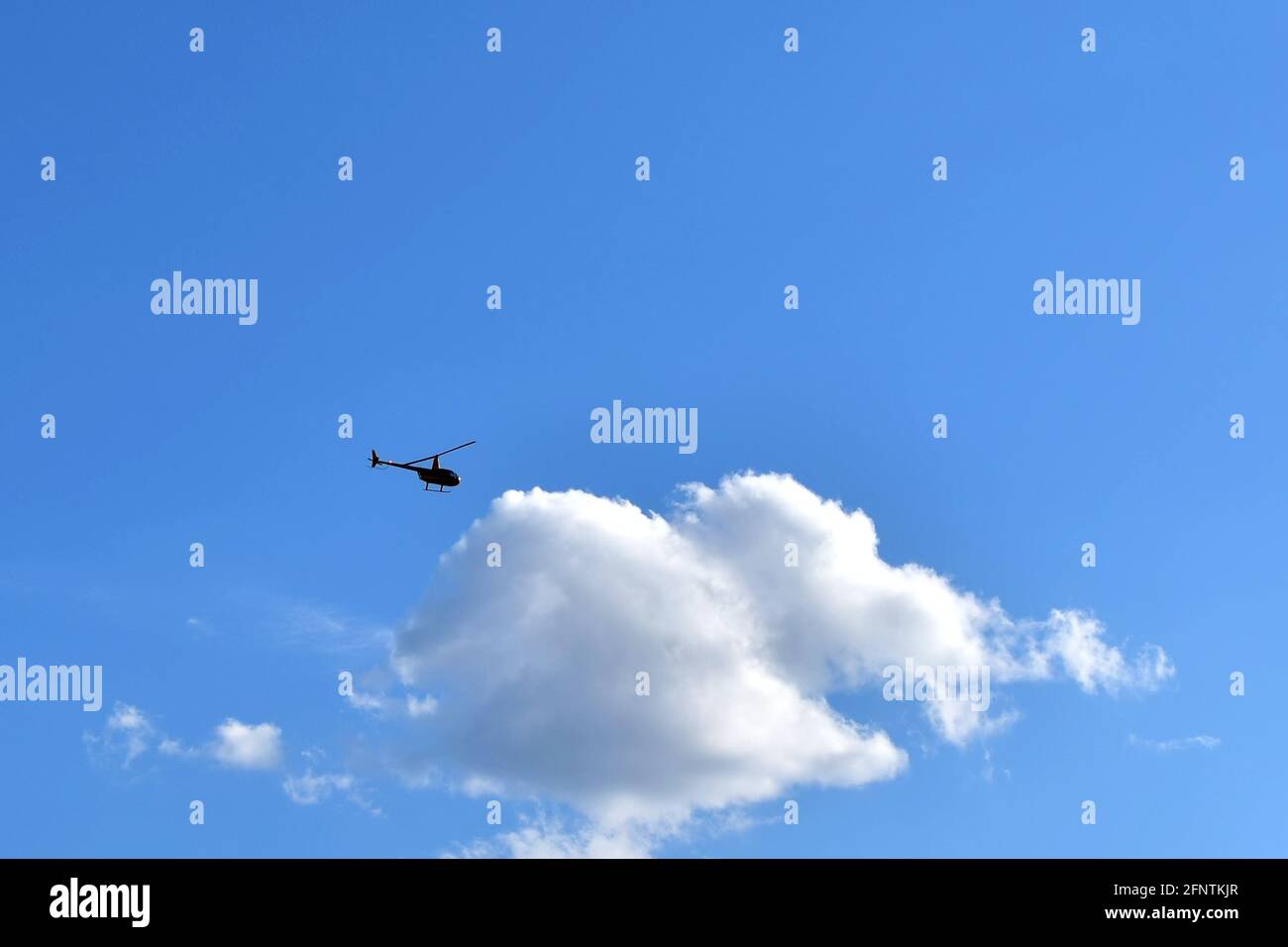 Kleine Silhouette des Hubschraubers gegen große weiße Wolke auf Blau Himmel Stockfoto