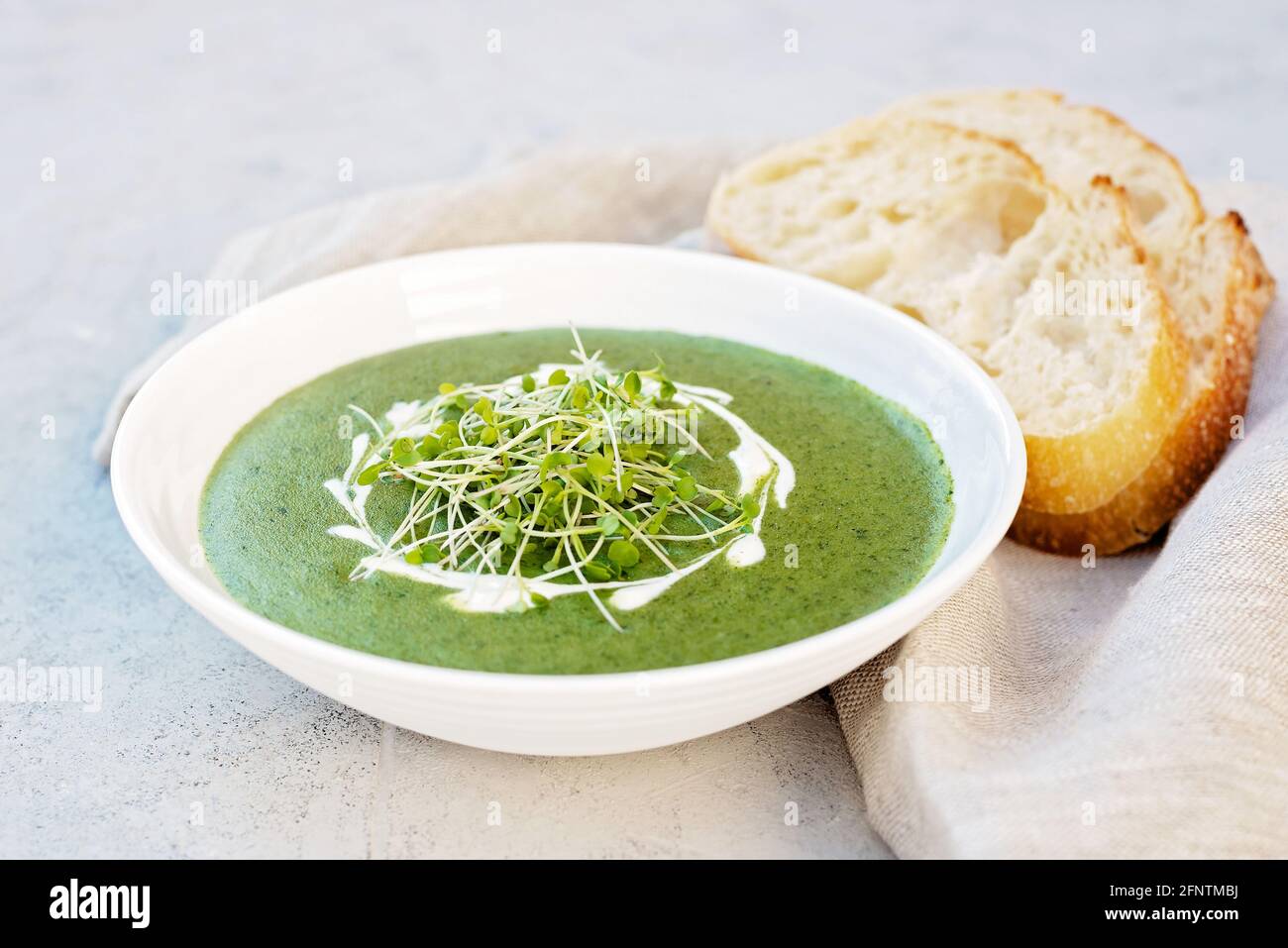 Suppe aus frischem Spinat mit Rahm und Rucola microgreen auf einem weißen Teller mit Ciabatta-Brot auf hellgrauem Hintergrund. Gesunde Ernährung und Ernährung. Stockfoto