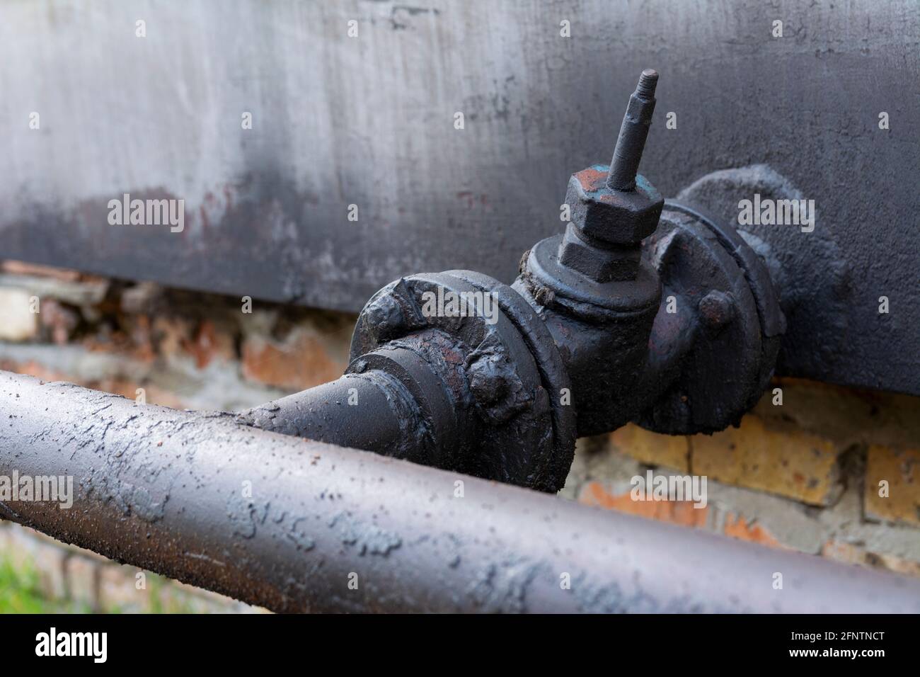 Rohr für Dieselkraftstoff oder Öl mit Ventil. Eine Schicht schwarzen getrockneten Brennstoffs auf einem alten Metallhahn. Stockfoto