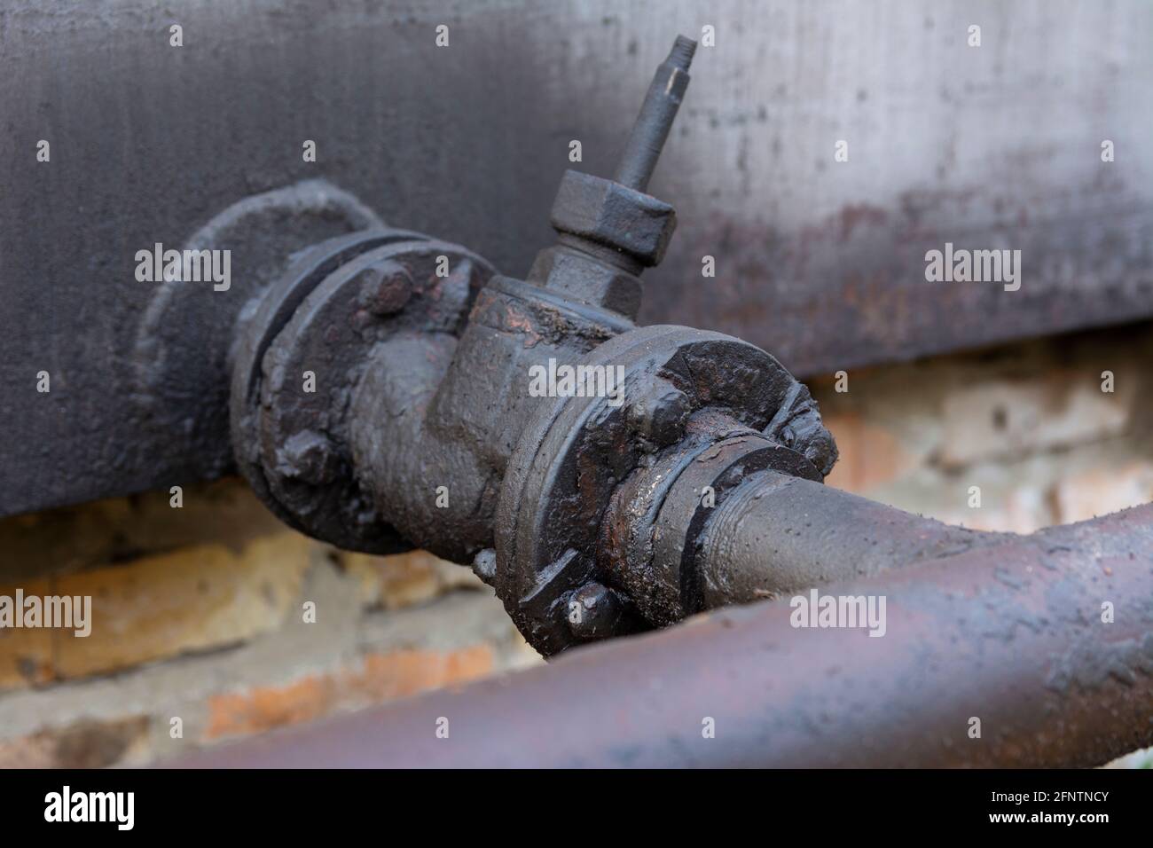 Rohr für Dieselkraftstoff oder Öl mit Ventil. Eine Schicht schwarzen getrockneten Brennstoffs auf einem alten Metallhahn. Stockfoto