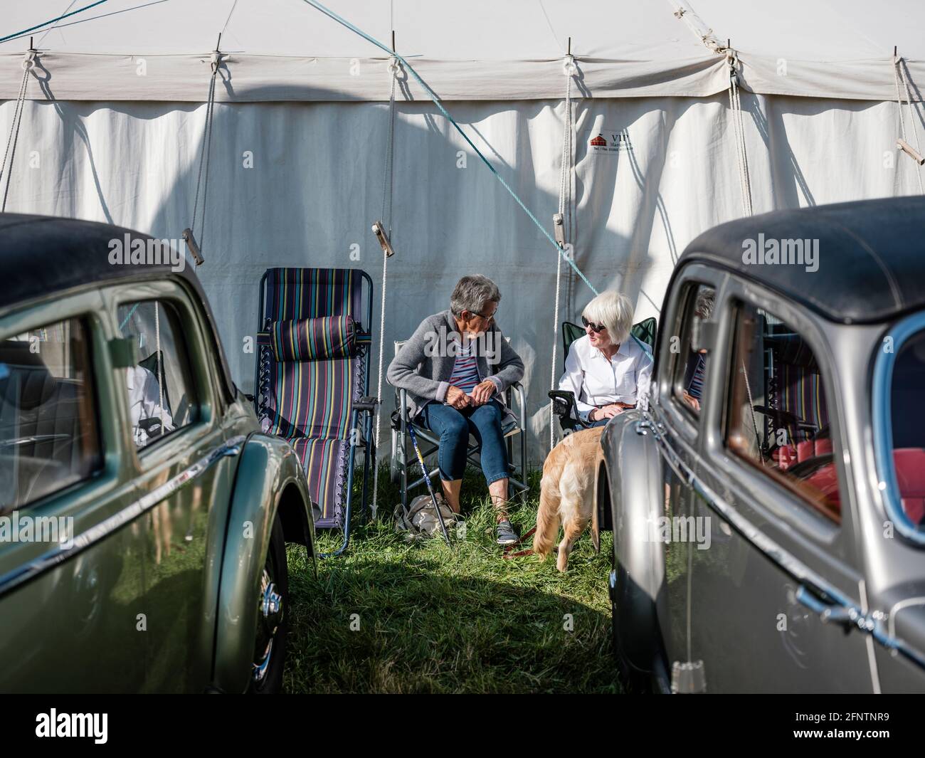 Zwei Frauen diskutieren auf der Melplash Agricultural Society Show auf dem West Bay Show Grounds, Bridport, Dorset, unter ein paar Oldtimern Stockfoto