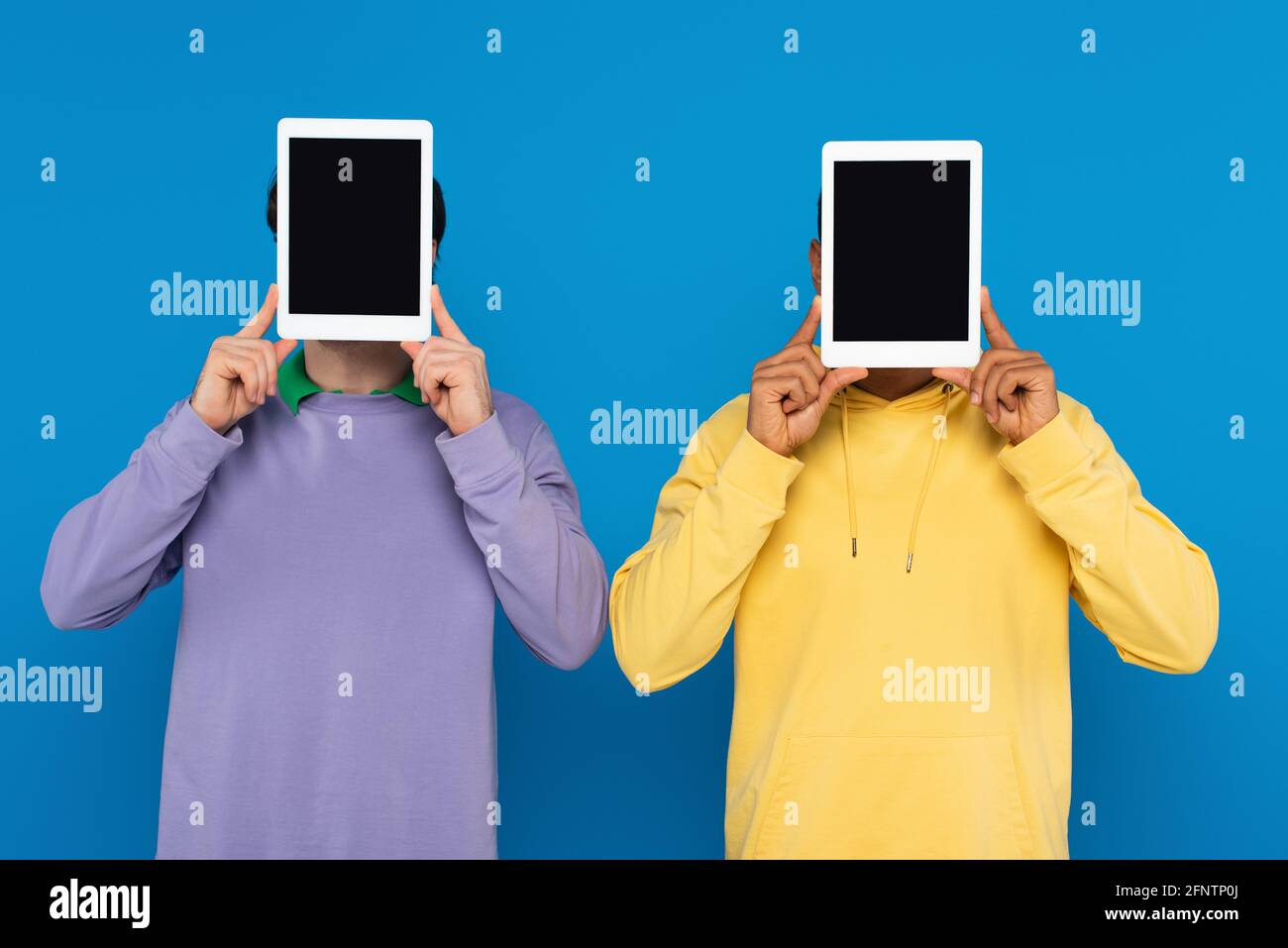 Interracial Freunde mit obskuren Gesichtern halten digitale Tabletten mit leer Bildschirm auf blau isoliert Stockfoto