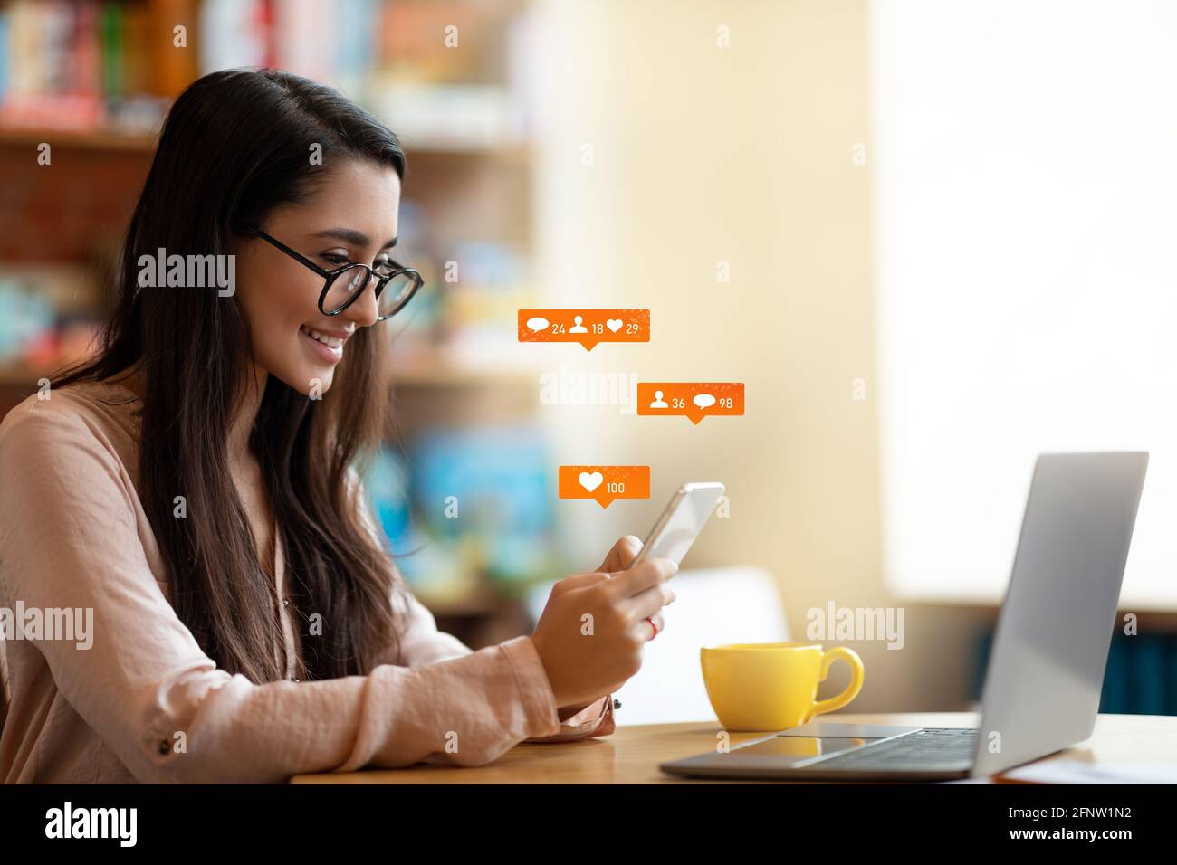 Glückliche lateinische Bloggerin mit Smartphone mit Social-Media-Benachrichtigungssymbolen, sitzen im Café, freier Platz. Stockfoto