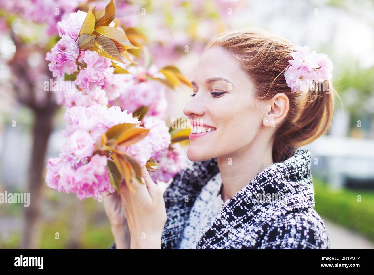 Glückliche junge natürliche Frau, die während der Sakura im Freien Kirschblüte hält Stockfoto