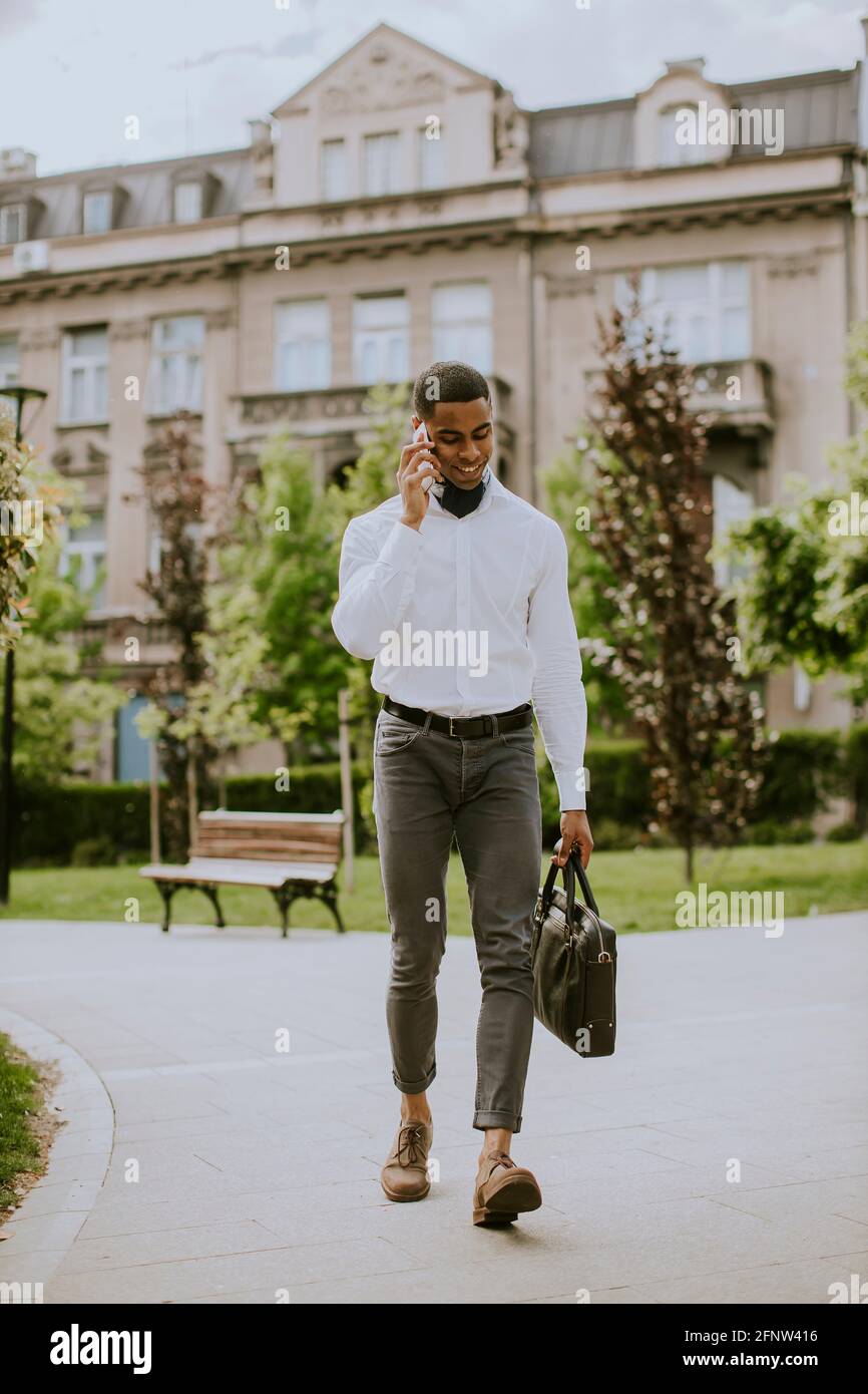Hübscher junger afroamerikanischer Geschäftsmann, der ein Mobiltelefon verwendet Eine Straße Stockfoto
