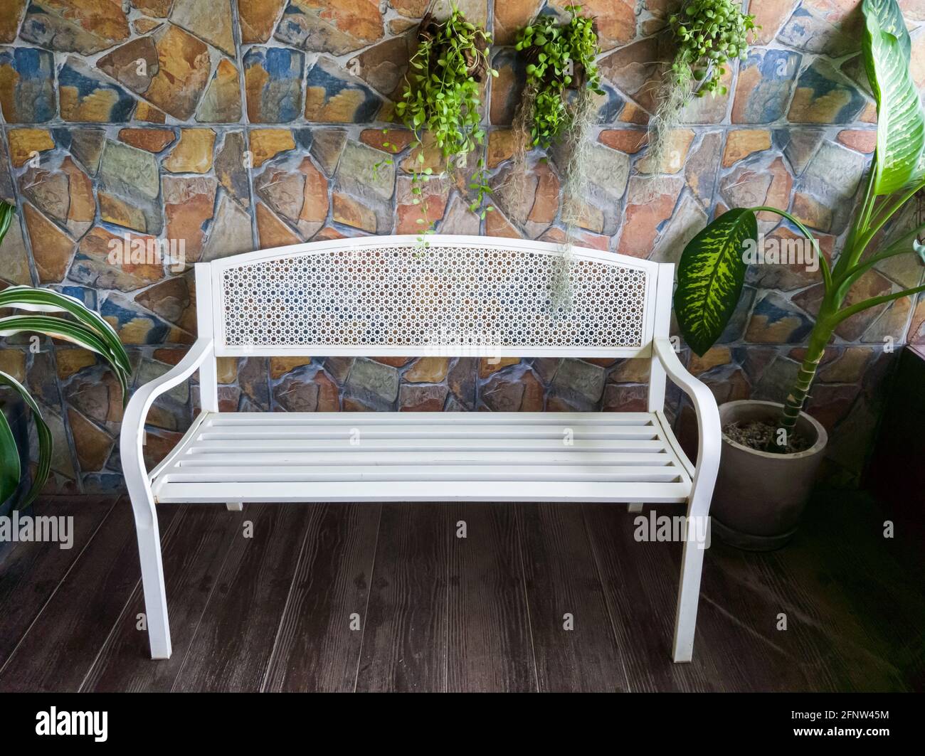 Die leere weiße Metallbank im Retro-Stil in der Nähe der Holzterrasse und dekoriert mit der Pflanze für die Entspannung des lokalen Bistro, Vorderansicht Stockfoto