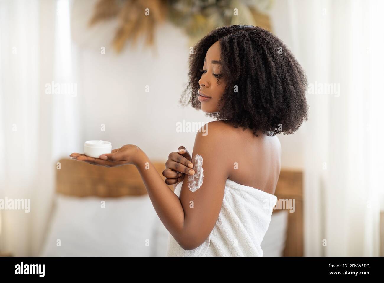 Schönheitsbehandlung für gesunde Haut. Wunderschöne schwarze Frau im  Badetuch Anwendung Körpercreme oder Butter auf der Schulter zu Hause  Stockfotografie - Alamy