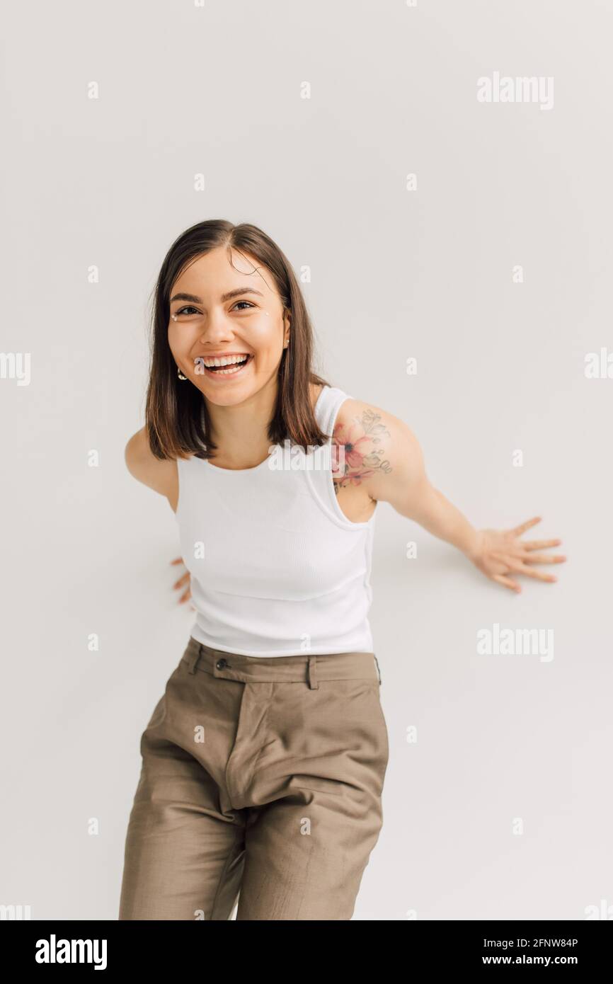 Lachende junge Frau im weißen Oberteil und beige Hose an Grauer Hintergrund Stockfoto