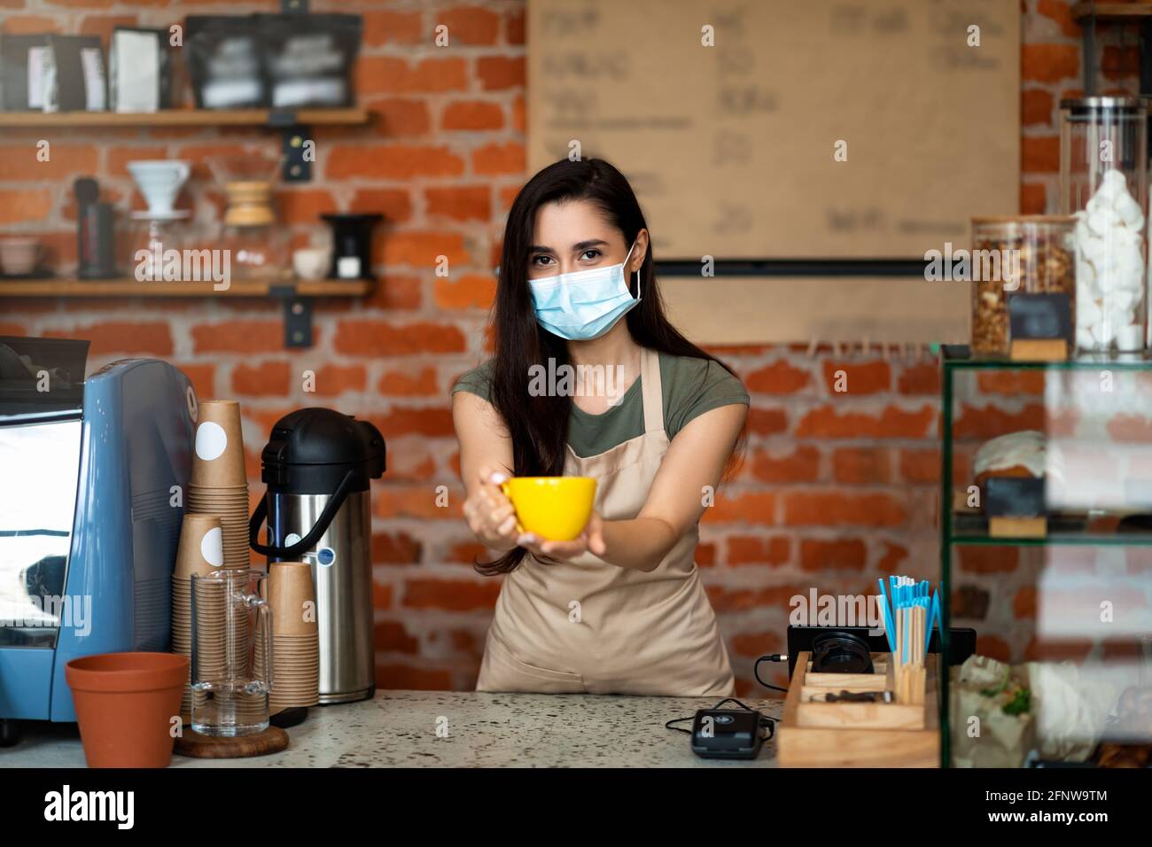 Ein fröhlicher Barista begrüßt die Gäste in der eigenen Cafeteria, bietet heiße Getränke an und kehrt nach der Pandemie des 19. September wieder zur Arbeit zurück Stockfoto