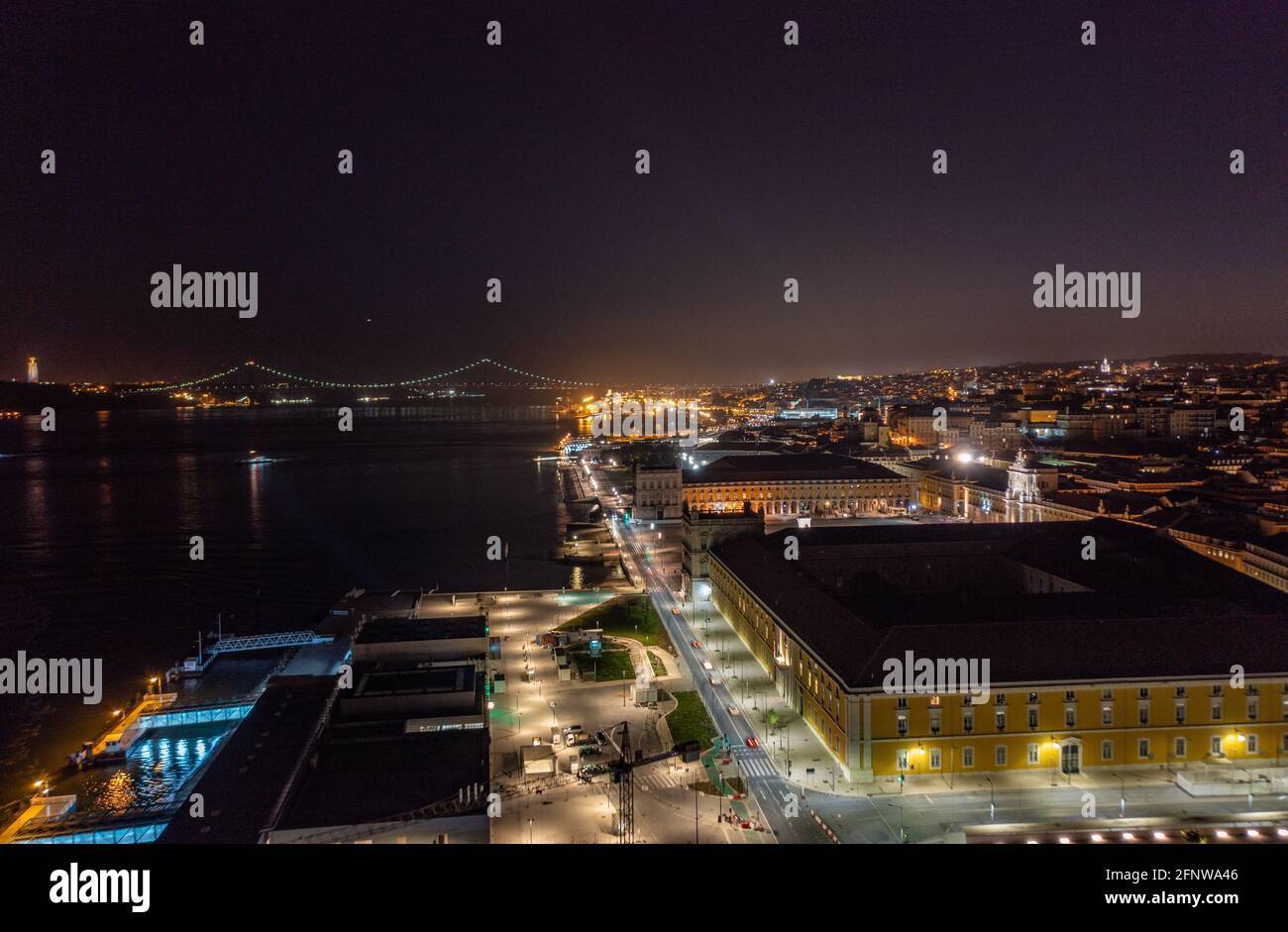 Drohnenansicht der Nachtstadt Lissabon, Portugal. Beleuchtete Gebäude am Flussufer. Leichte Kontur der Brücke im Hintergrund. Stockfoto