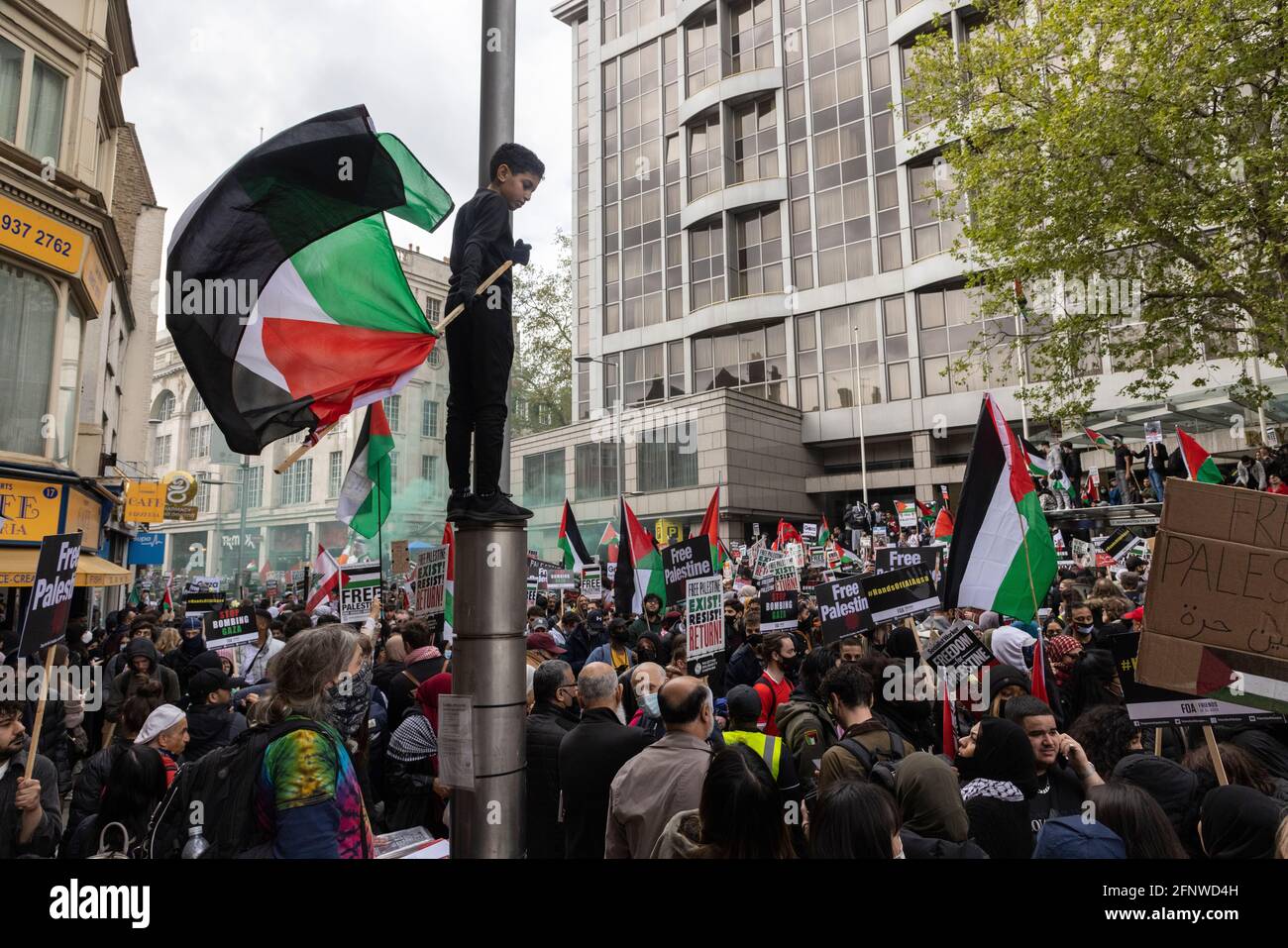 Ein Kind, das einen Lampenposten hochschwingend, Flagge über der Menge, Solidaritätsprotest „Free Palestine“, London, 15. Mai 2021 Stockfoto