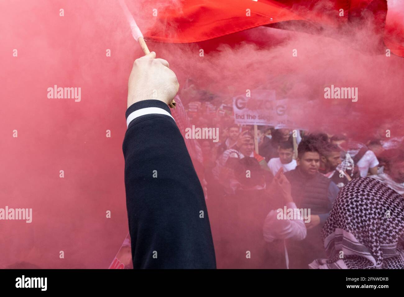 Ein Protestler schwenkt rote Fahne zwischen farbigem Rauch, Solidaritätsprotest „Free Palestine“, London, 15. Mai 2021 Stockfoto