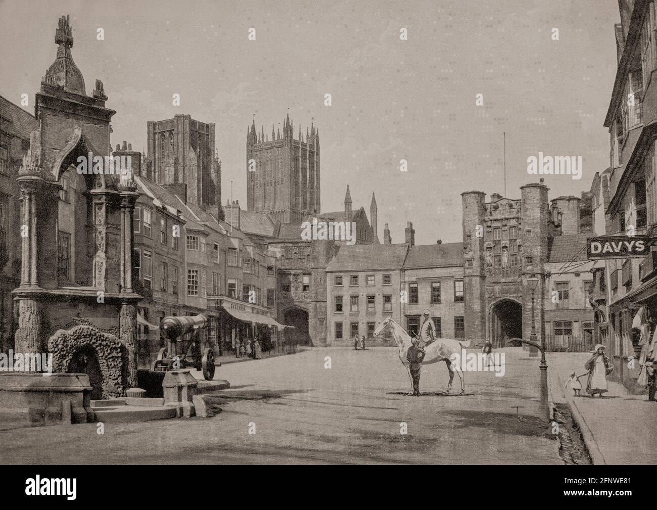 Eine Ansicht des Market Place aus dem späten 19. Jahrhundert in Wells, einer Stadt im Mendip-Viertel von Somerset, England. Der Market Place, ein Ort eines der alten Brunnen der Stadt (man beachte das Wasser, das in der Schlucht neben dem Bürgersteig fließt); das Bishop's Eye Torhaus (zum Bishop's Palace) befindet sich am anderen Ende; zwei der Türme der Wells Cathedral sind hinter den Gebäuden zu sehen. Stockfoto