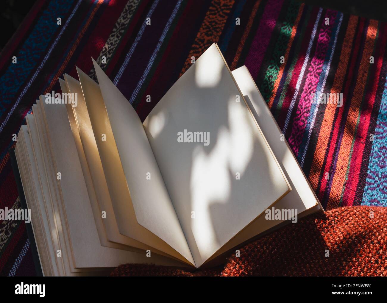Abbildung eines offenen Notizbuchs mit leeren Seiten Ein Tisch mit einer bunten Tischdecke in der Sonne Stockfoto