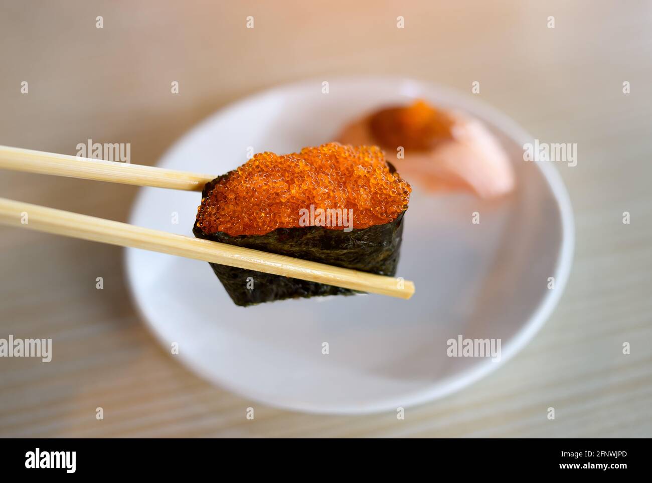 Gunkan Sushi aus Tobiko fliegender Fischrogen im Essstäbchen mit dezenter Beleuchtung in Innenräumen. Stockfoto