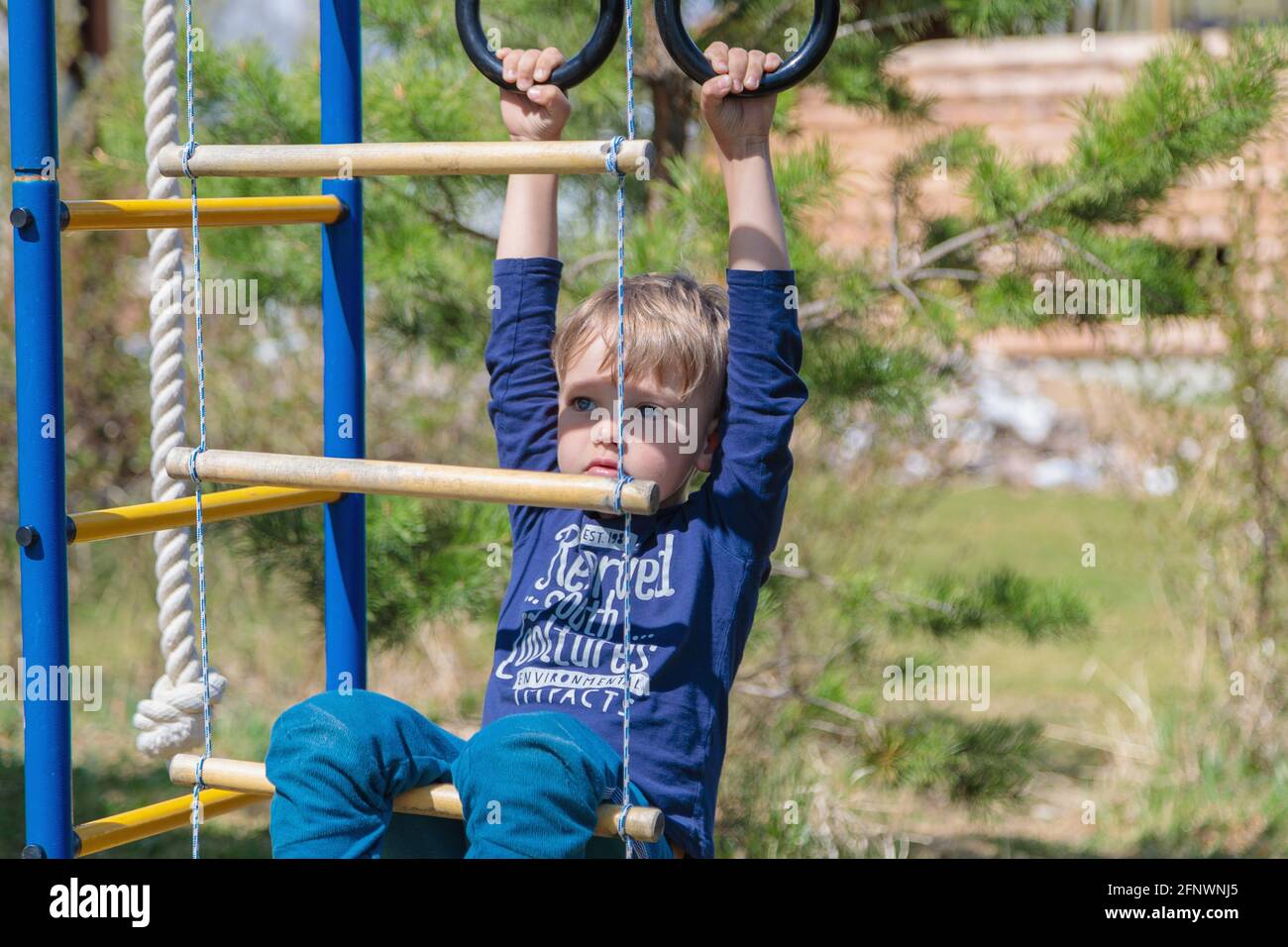Ein blondes Kind spielt auf dem Spielplatz, hängt an Ringen. Stockfoto