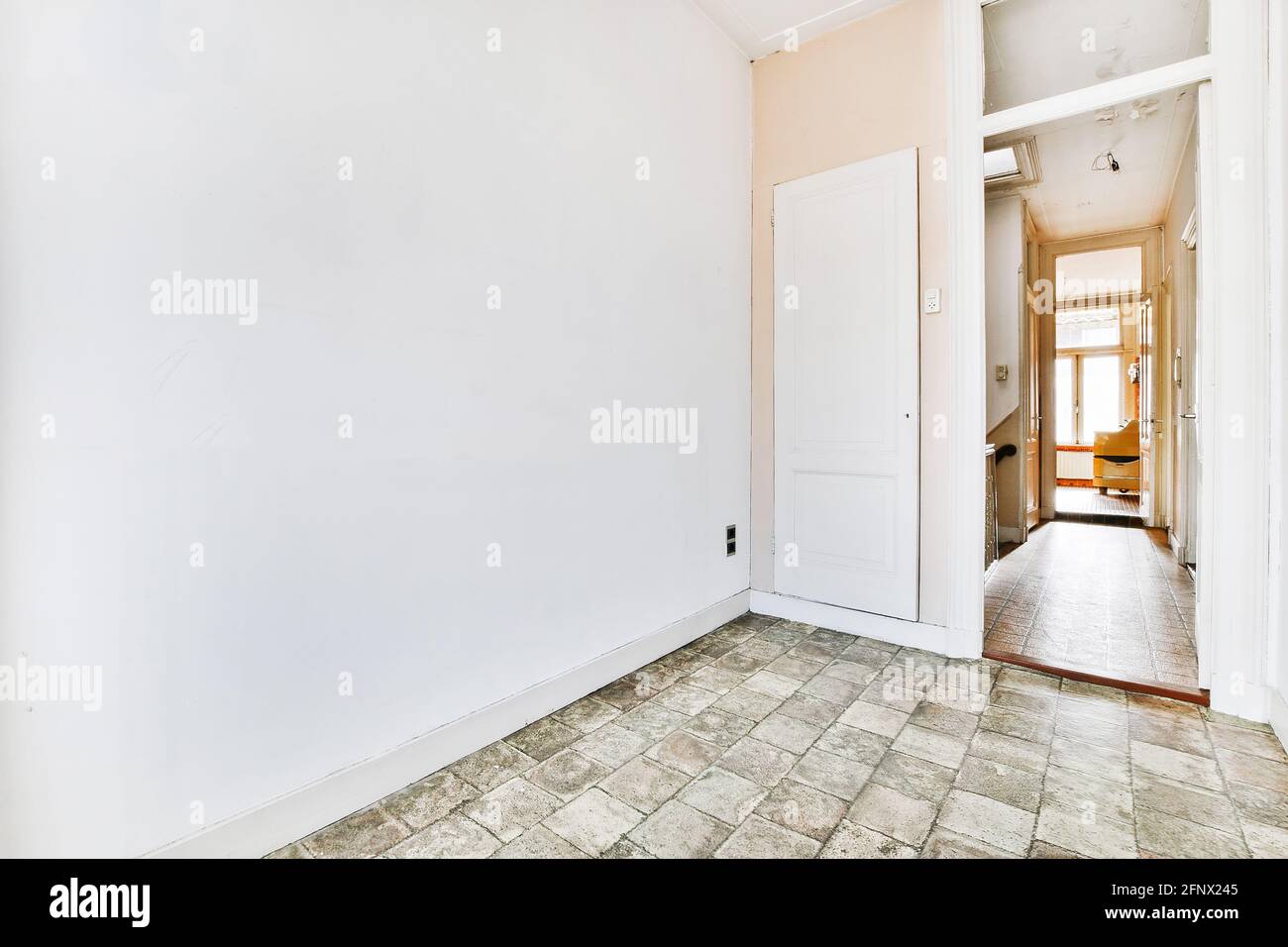 Fragment des Innenraums des leeren Raumes mit gefliestem Fußboden und Schranktür in altmodischer Wohnung mit schmalen Korridor und Weiße Wände Stockfoto