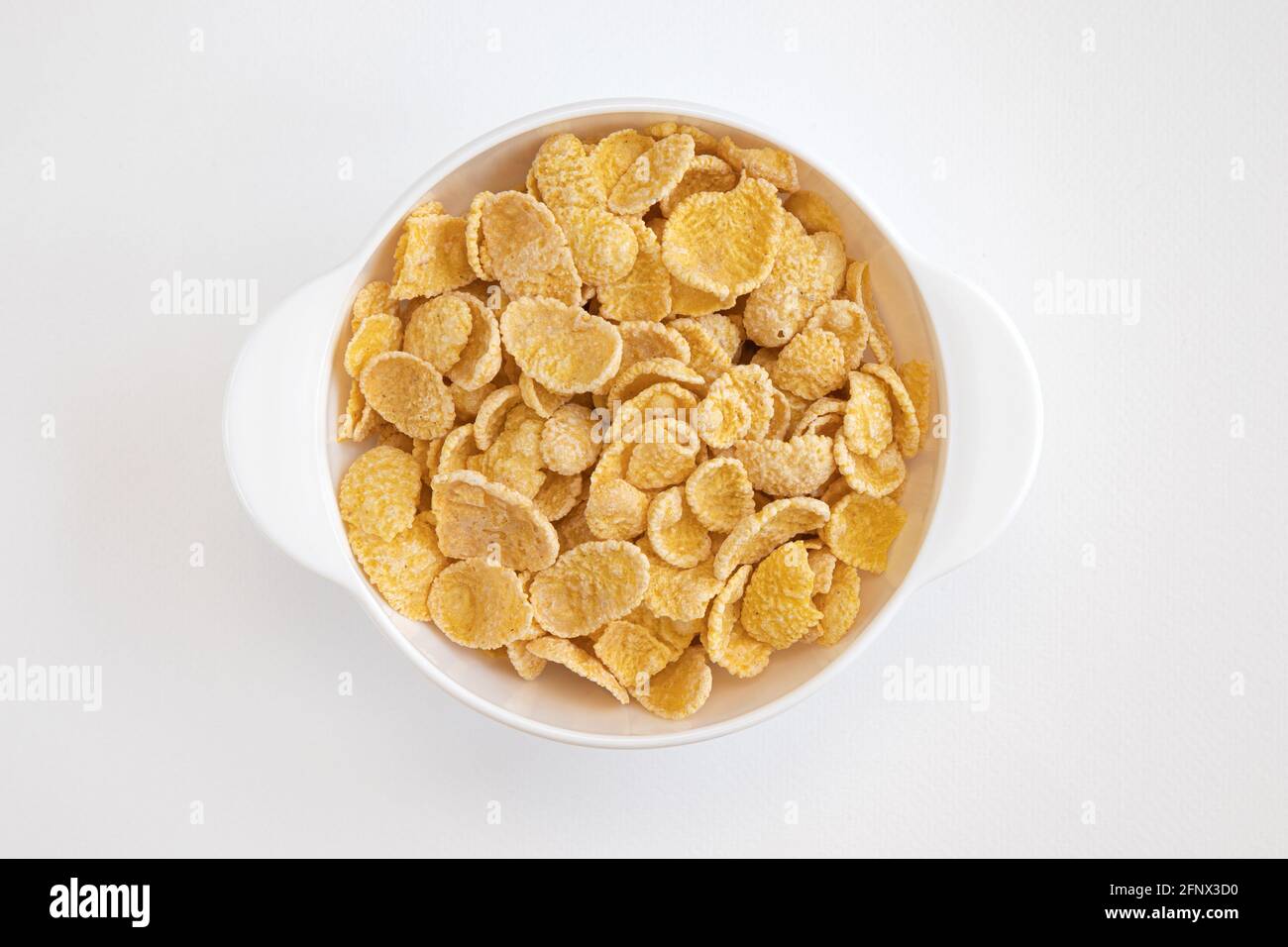 Maisflocke in Schüssel auf weißem Hintergrund, Teller mit Cornflakes, gesundes Frühstückskonzept, um die Tasse zerbröckelte Maisflocken, Draufsicht Stockfoto