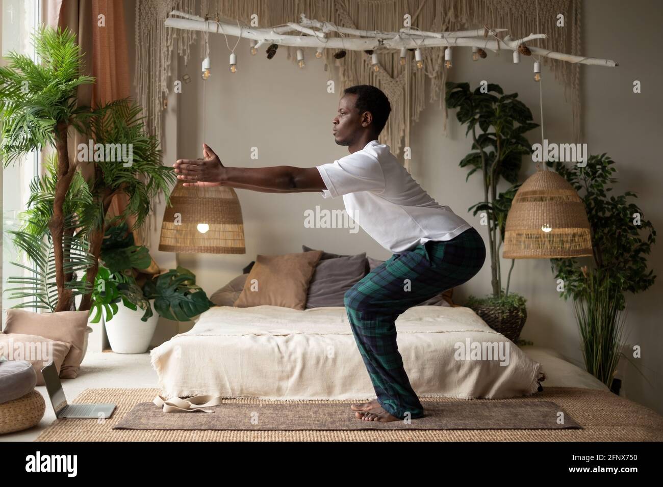 Afrikanischer junger Mann, der in einem Rückzugsraum Yoga praktiziert Doing Chair Pose oder Utkatasana Stockfoto