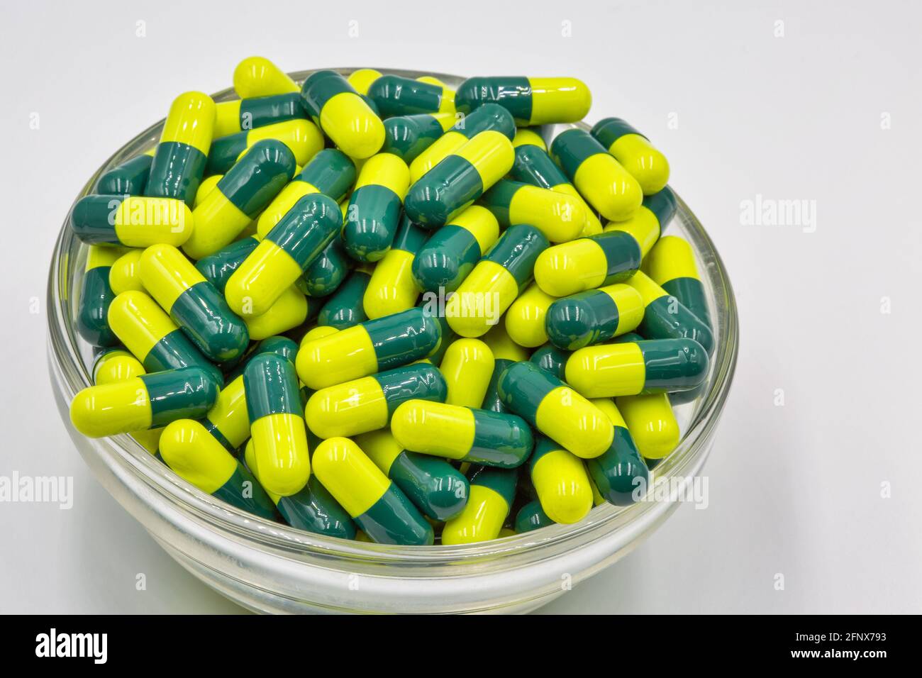 Medizinische Kapseln gelb grün in Glasschale Nahaufnahme gegen weiß Hintergrund Stockfoto