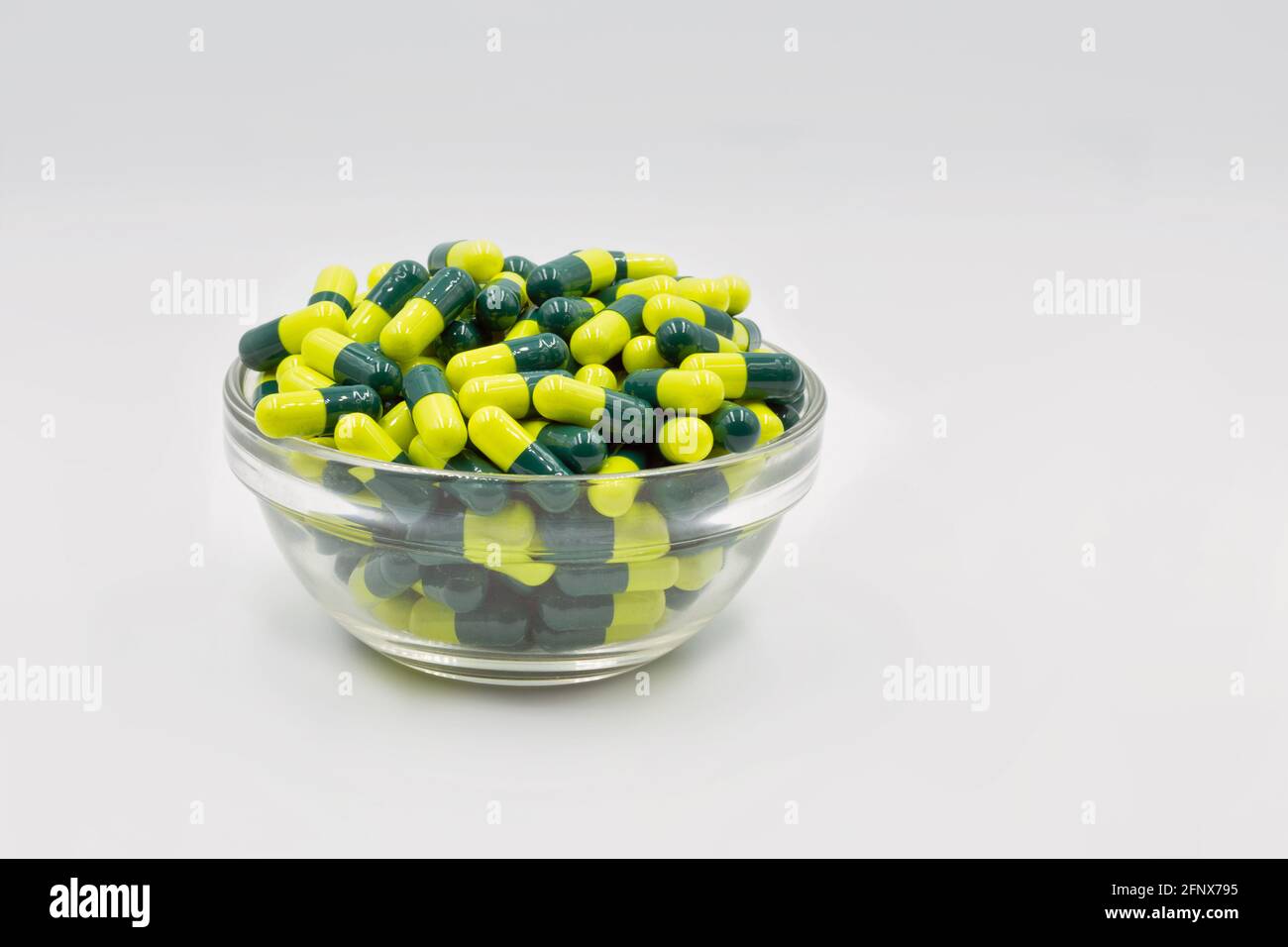Medizinische Kapseln gelb grün in Glasschale Nahaufnahme gegen weiß Hintergrund Stockfoto
