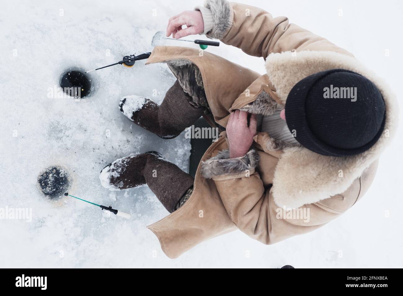 Ein Fischer im Winter Angeln in warmen Kleidern und Filz Stiefel Stockfoto