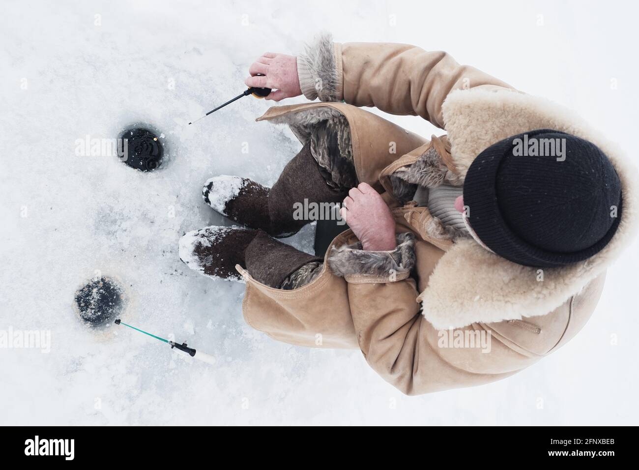 Ein Fischer, der im Winter in warmen Kleidern und Filzstiefeln fischt. Stockfoto