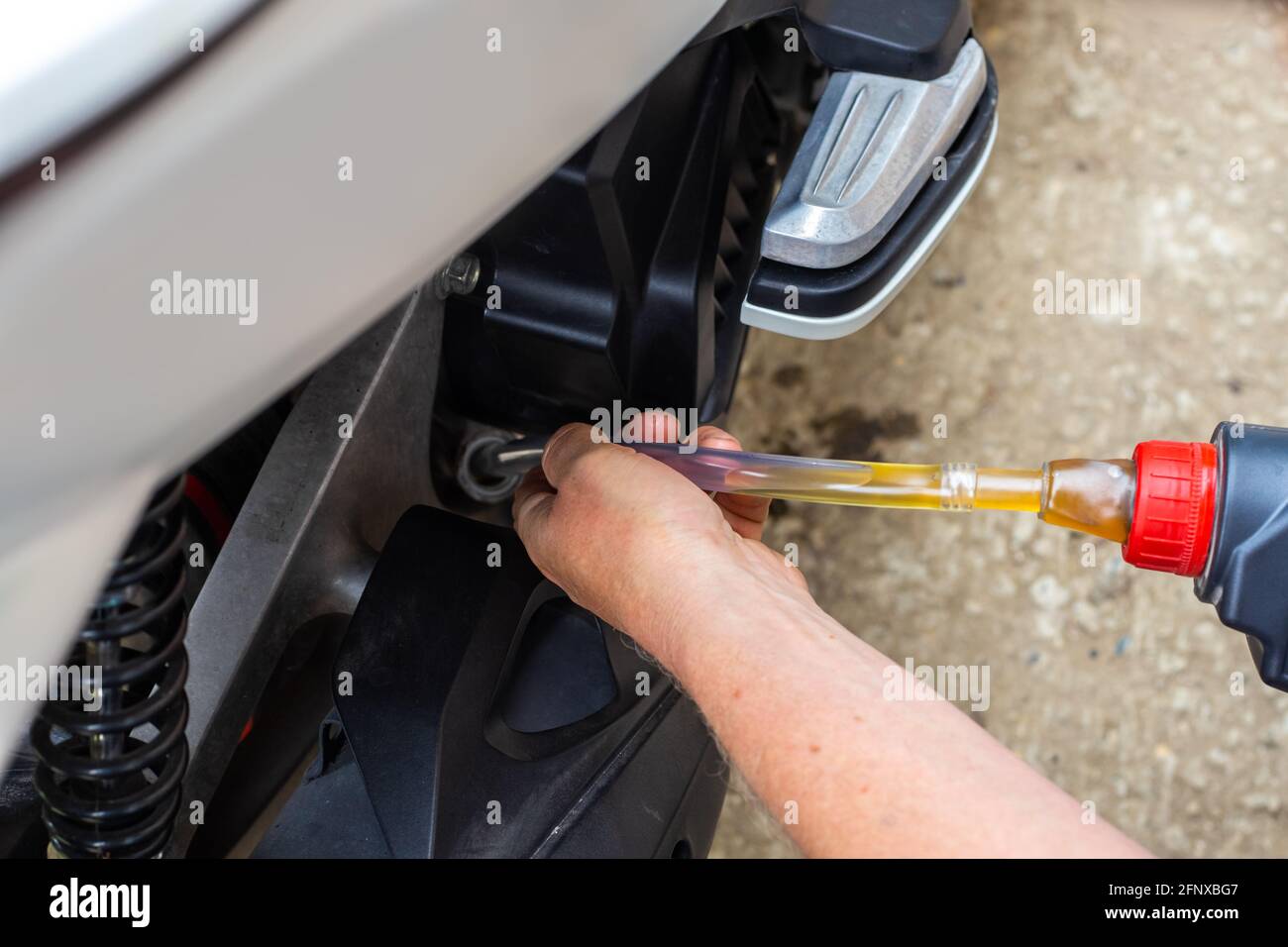 Reparatur und Wartung eines Motorrads. Ölwechsel. Der Automechaniker gießt Öl über einen Gummischlauch in den Motor. Stockfoto