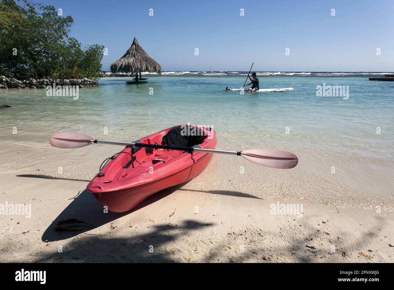 Rotes Kajak am Strand, Paddelbrett im Hintergrund. Karibik Authentic Reisen in Roatan Honduras Stockfoto