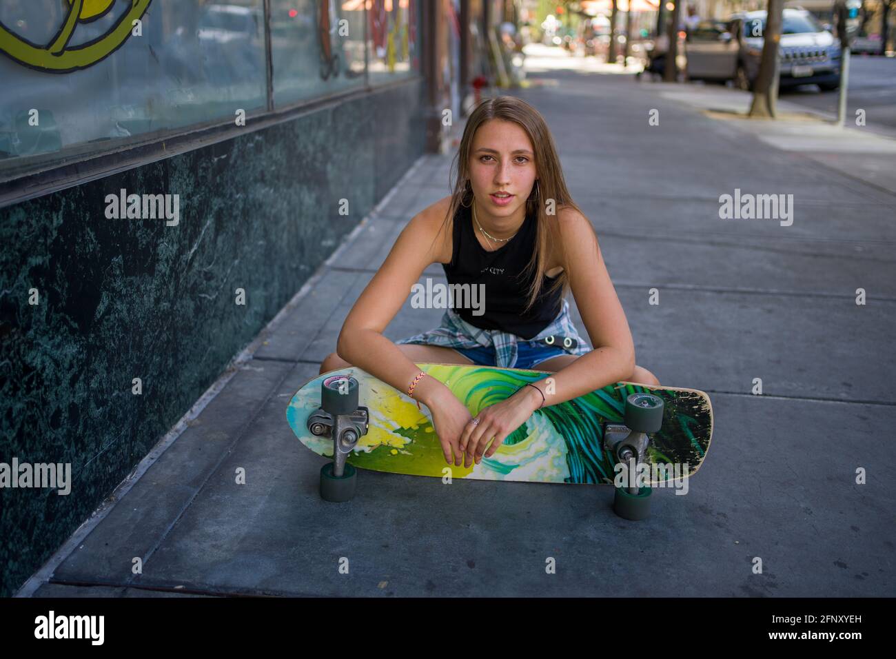 Junge Frau sitzt mit Skateboard in Downtown Urban Setting Stockfoto