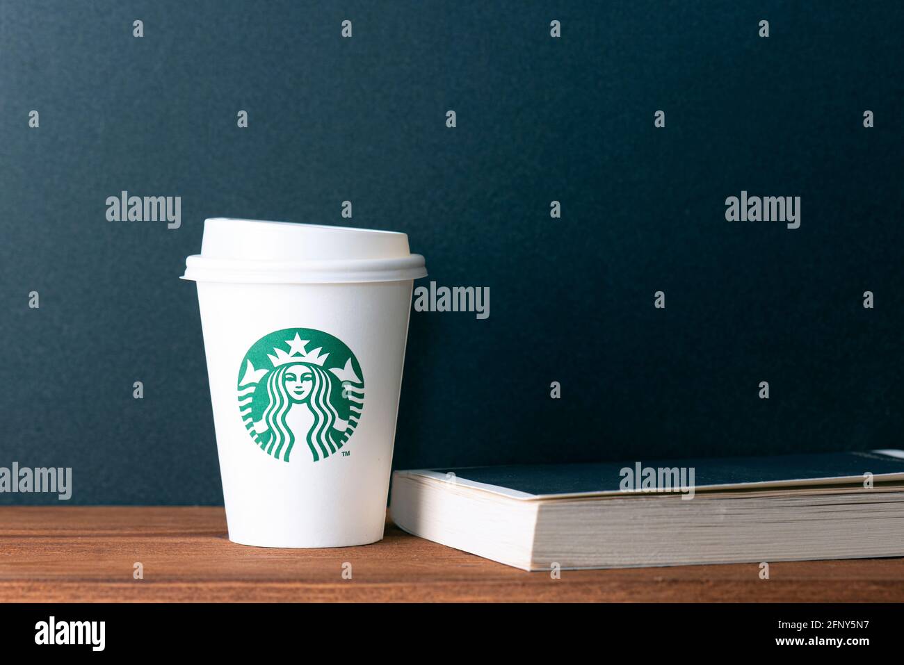 BERLIN - MAI 19: Weißer Becher aus Papier mit Starbucks-Logo und Buch auf Holztisch in Berlin, Mai 19. 2021 in Deutschland. Stockfoto
