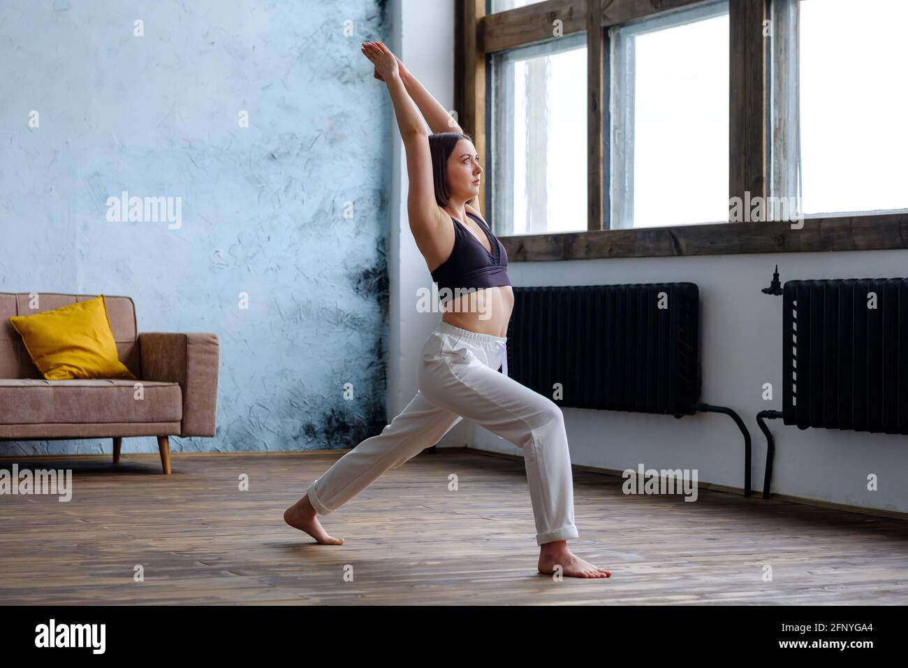 Frau in ihrem Wohnzimmer in Krieger-Yoga-Pose. Stockfoto