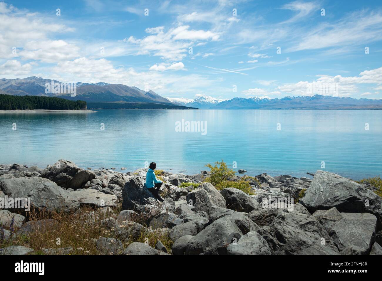 Frau, die am Ufer des Lake Pukaki sitzt und die Aussicht auf Mt Cook und die südlichen Alpen, Südinsel, genießt. Stockfoto