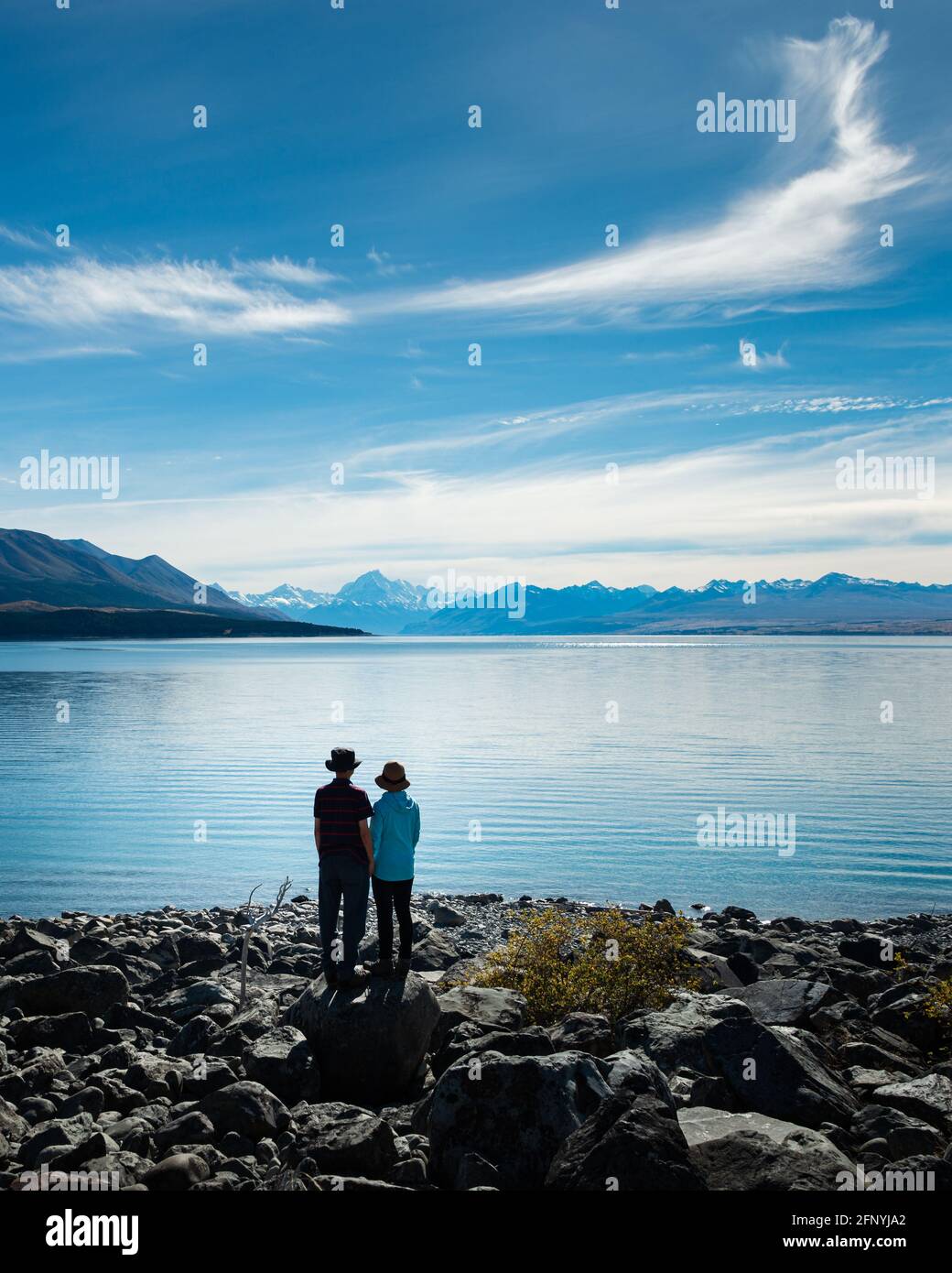 Pärchen, die am Ufer des Lake Pukaki stehen und die Aussicht auf Mt Cook und die südlichen Alpen, Südinsel, genießen. Vertikales Format. Stockfoto