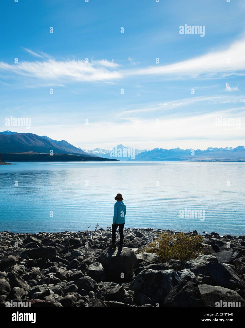 Frau, die am Ufer des Lake Pukaki steht und die Aussicht auf Mt Cook und die südlichen Alpen, Südinsel, genießt. Vertikales Format. Stockfoto